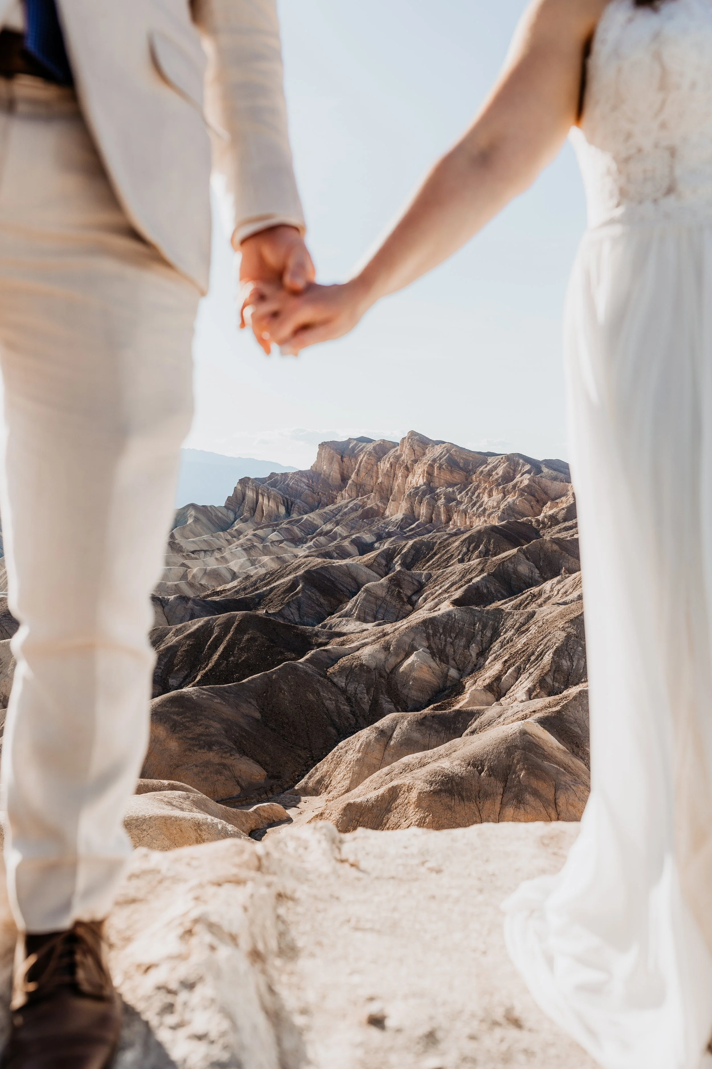 A couple holding hands in wedding attire standing on rocky terrain at death valley national park for elopement photos