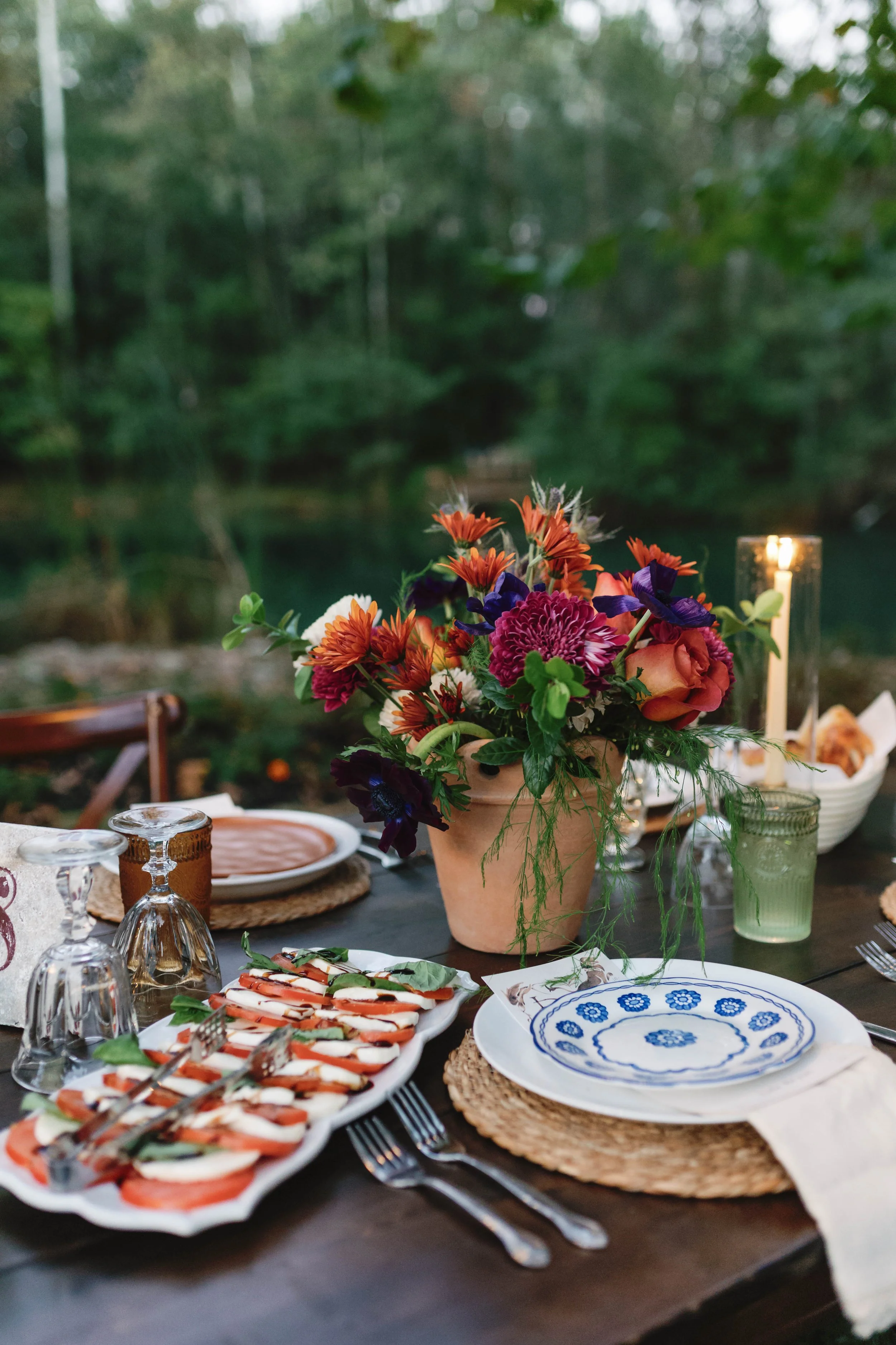 A table set outdoors with a floral centerpiece, plates, glasses, and a candle, with a lake and trees in the background. elegant kentucky backyard wedding 