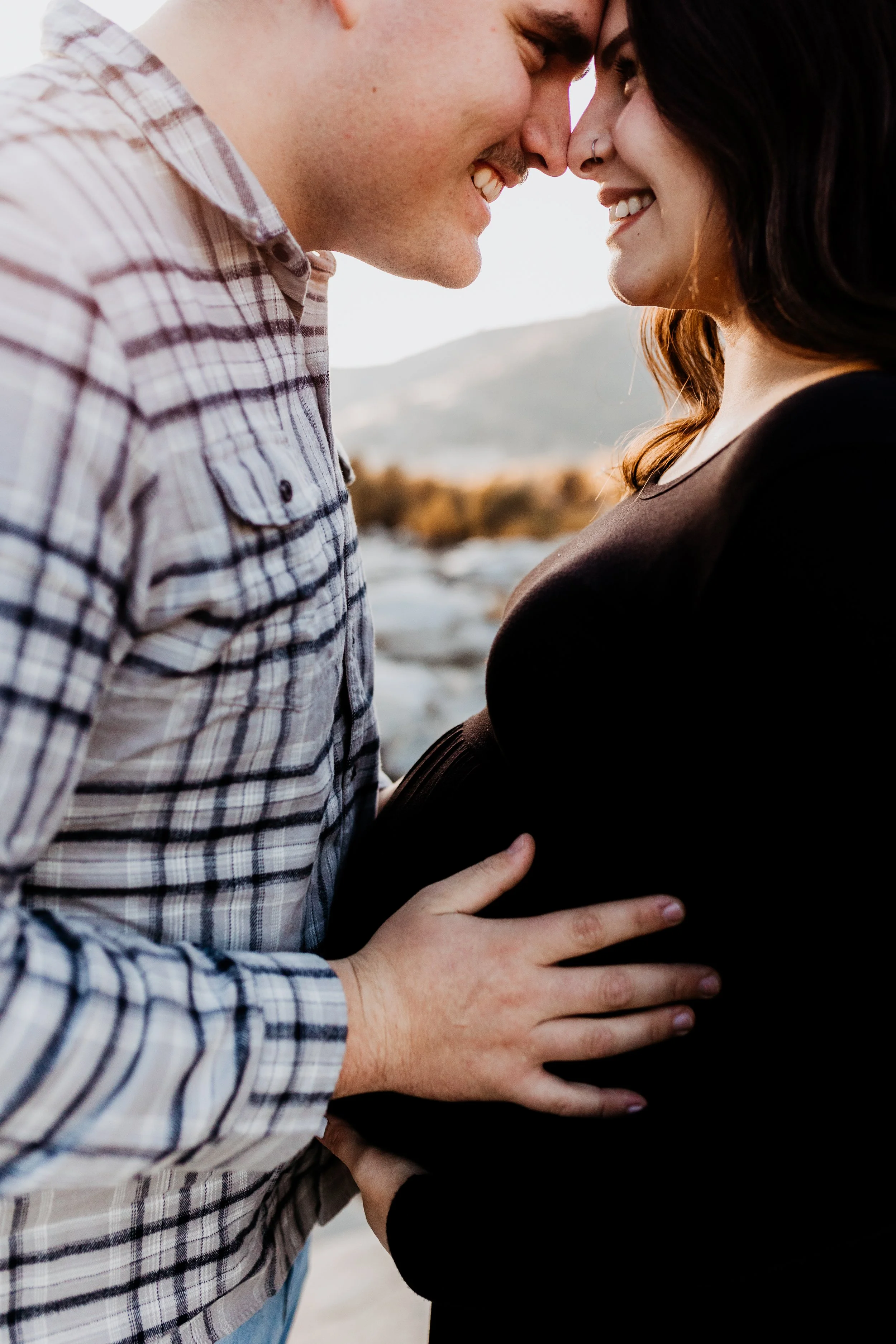 A man and woman touching foreheads and smiling outdoors, with mountains in the background.  lexington kentucky family photographer storytelling portraits maternity