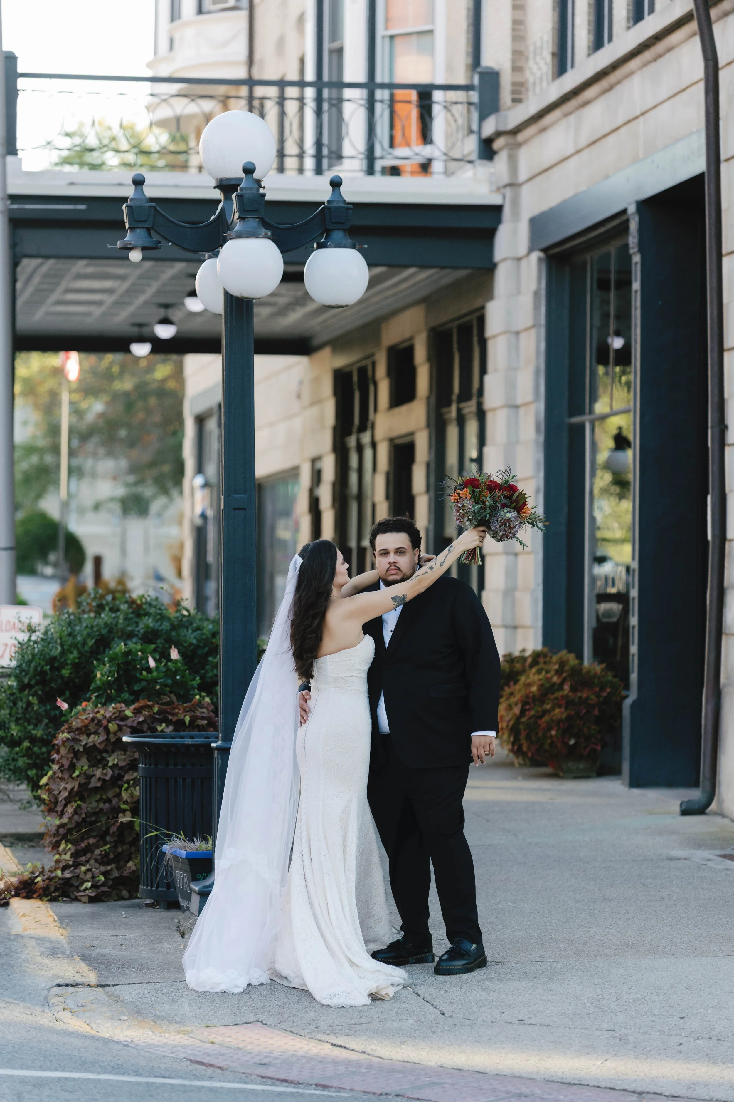 A newlywed couple stands on a city sidewalk, with the bride holding a bouquet of flowers above the groom's head. winchester opera house historic wedding kentucky 