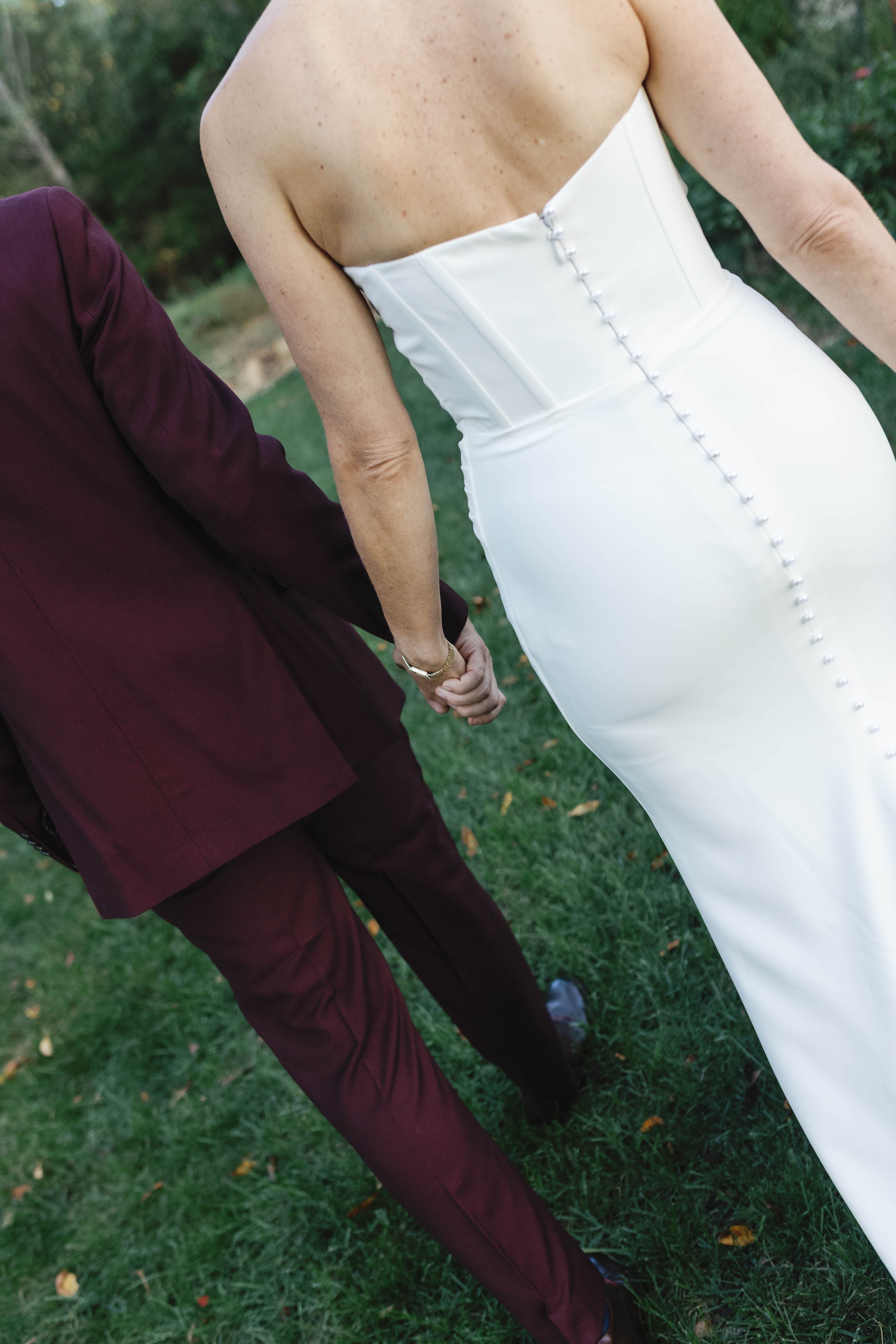 A bride and groom holding hands, walking outdoors on grass during their wedding.
