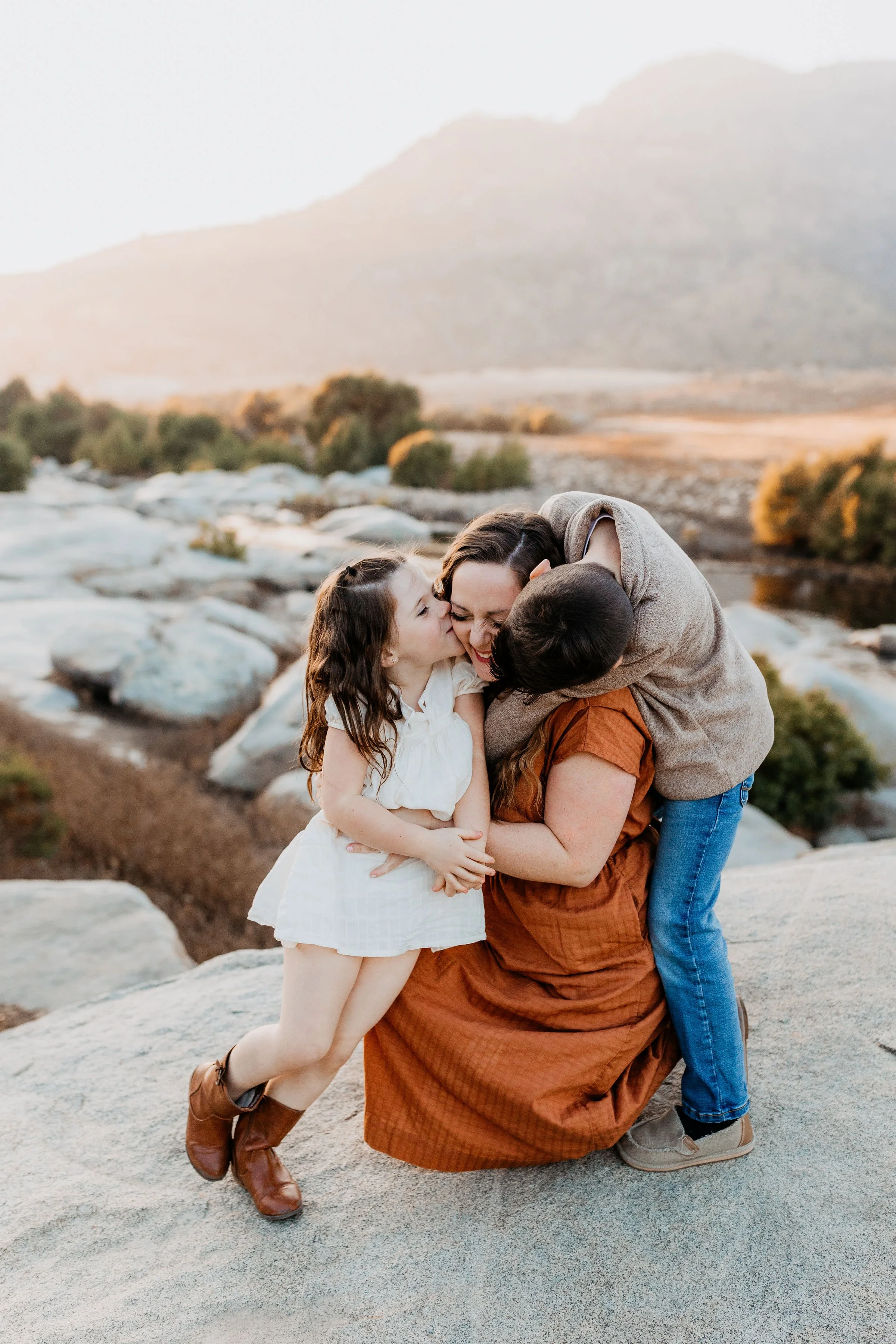 Three people hugging outdoors on rocks with mountains and river in the background at sunset.  lexington kentucky family photographer storytelling portraits