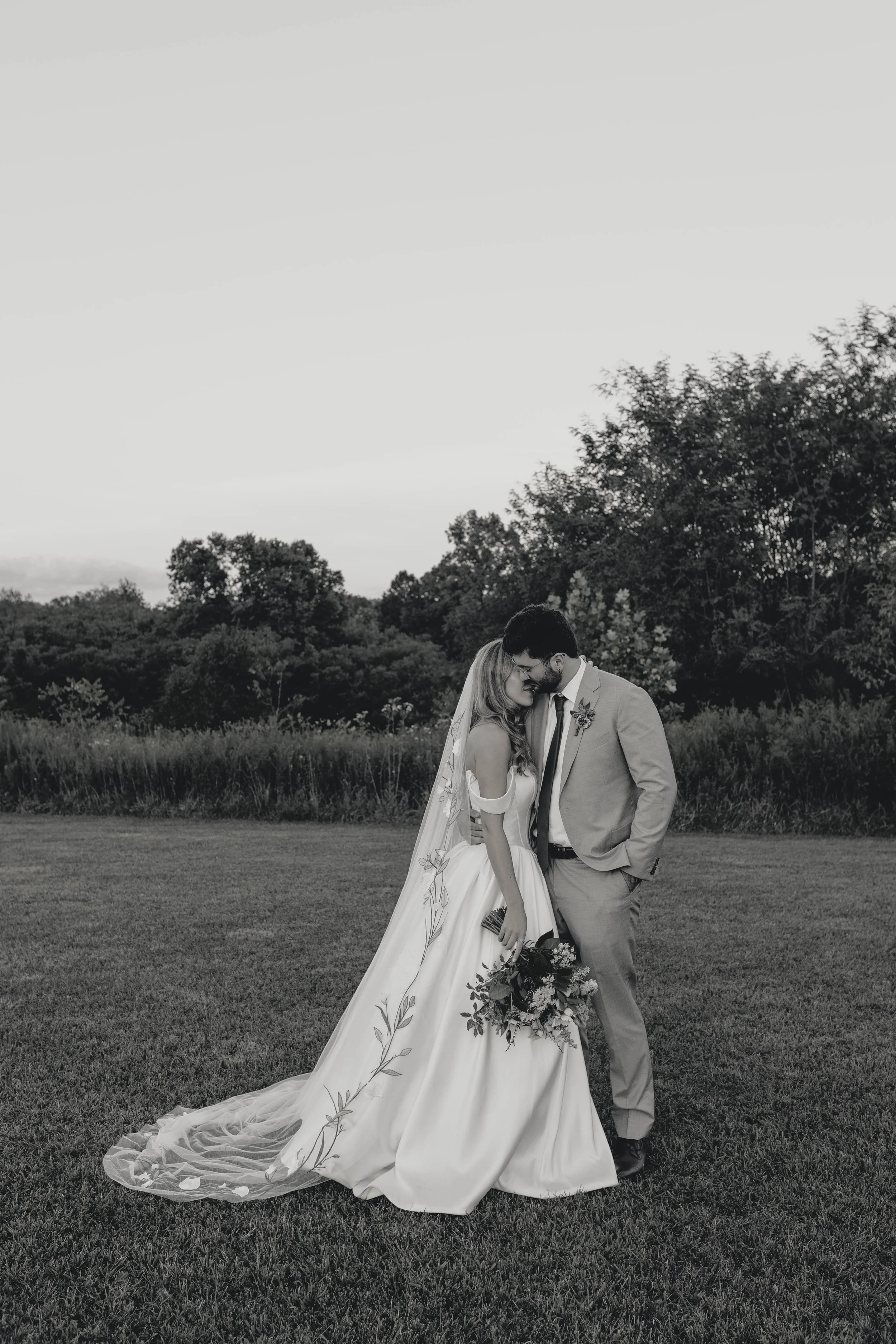 Black and white photo of a bride and groom standing close together outdoors on grass, smiling and touching foreheads. shaker village wedding harrodsburg kentucky