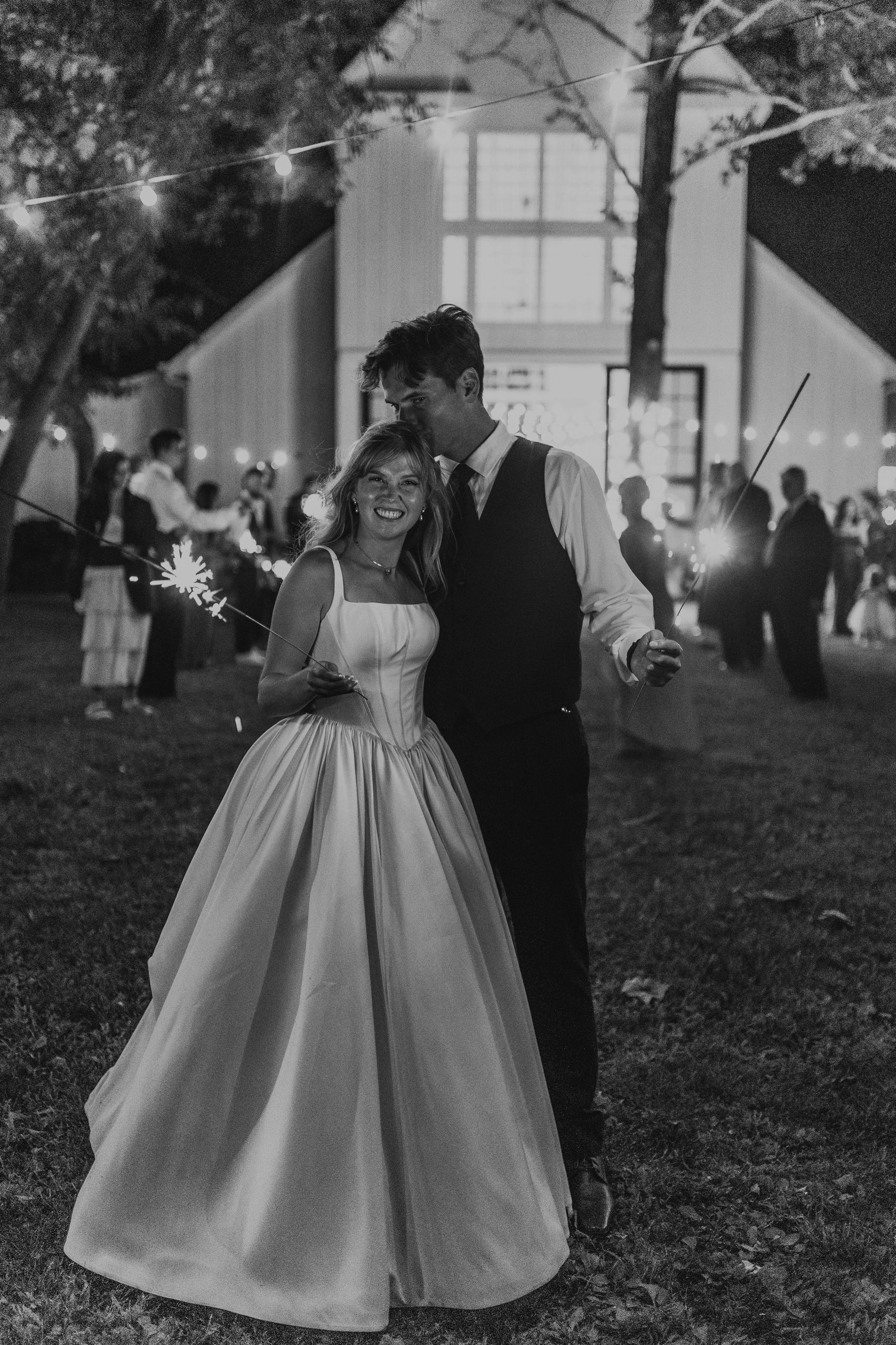 A bride and groom celebrating at night, holding sparklers, surrounded by wedding guests under outdoor string lights kentucky wedding and ashford acres in cynthiana kentucky