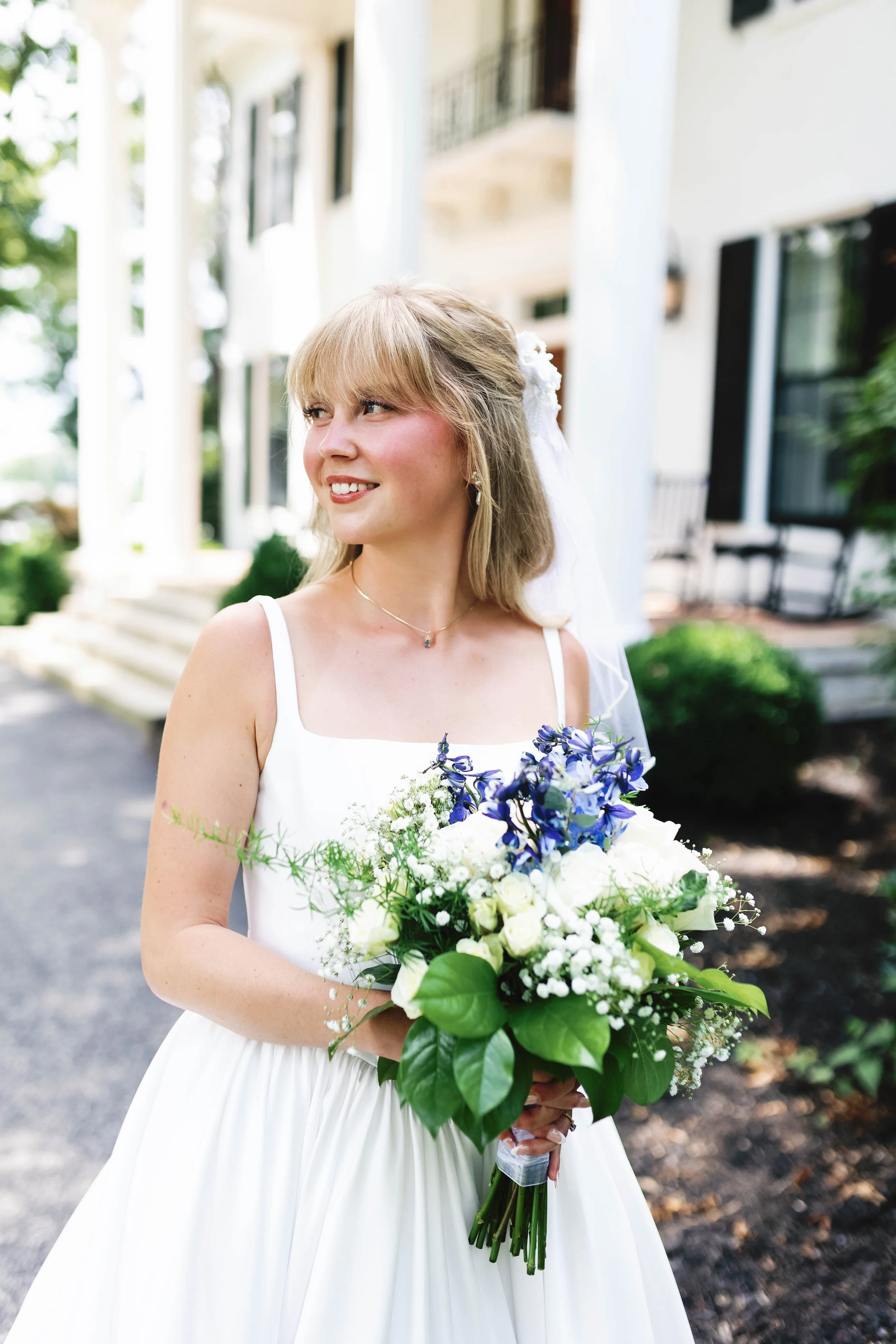 A bride in a white dress holding a bouquet of white and purple flowers outside of a house. ashford acres inn wedding cynthiana kentucky