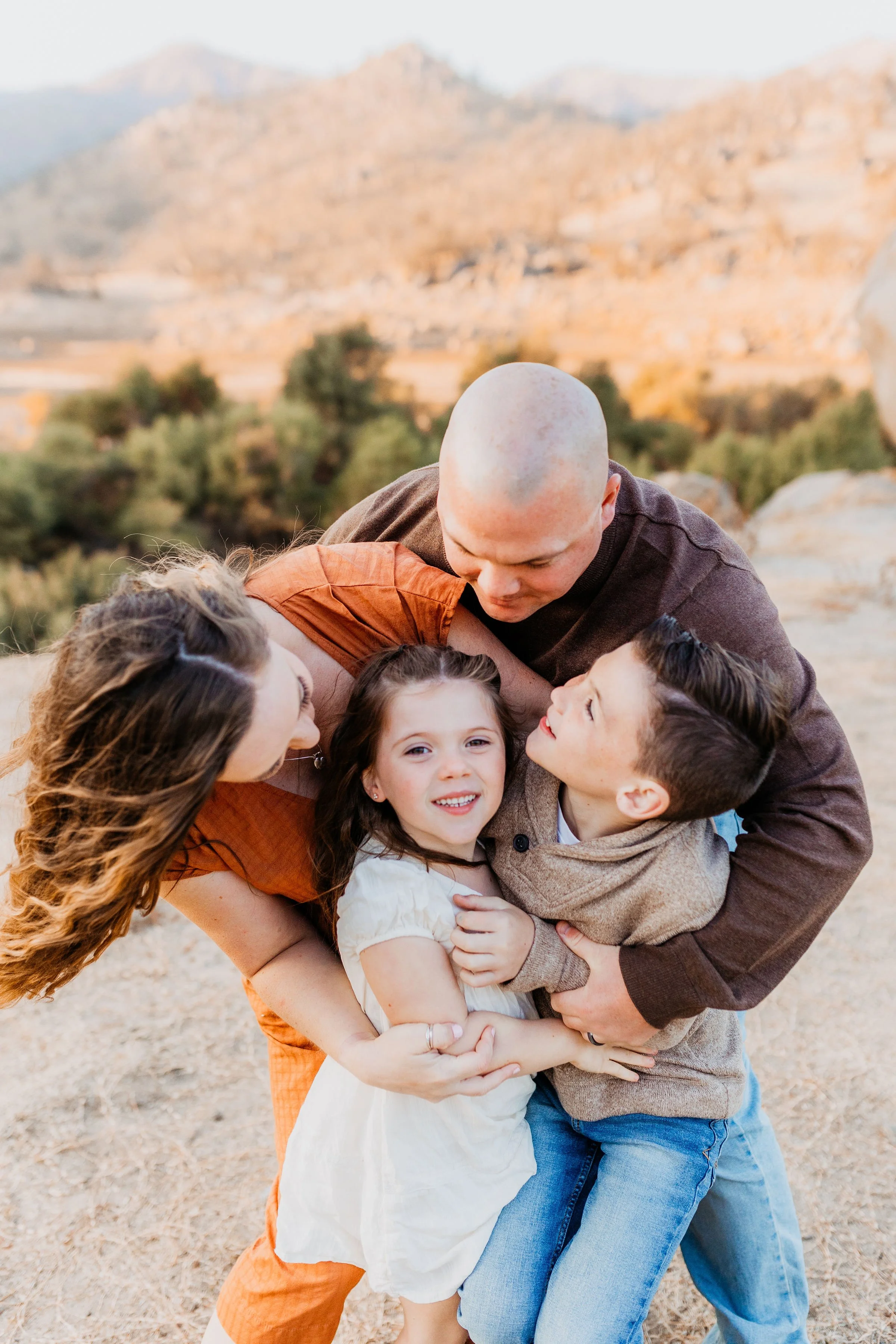 Family of four embracing outdoors in a desert landscape with hills in the background, during sunset.  lexington kentucky family photographer storytelling portraits