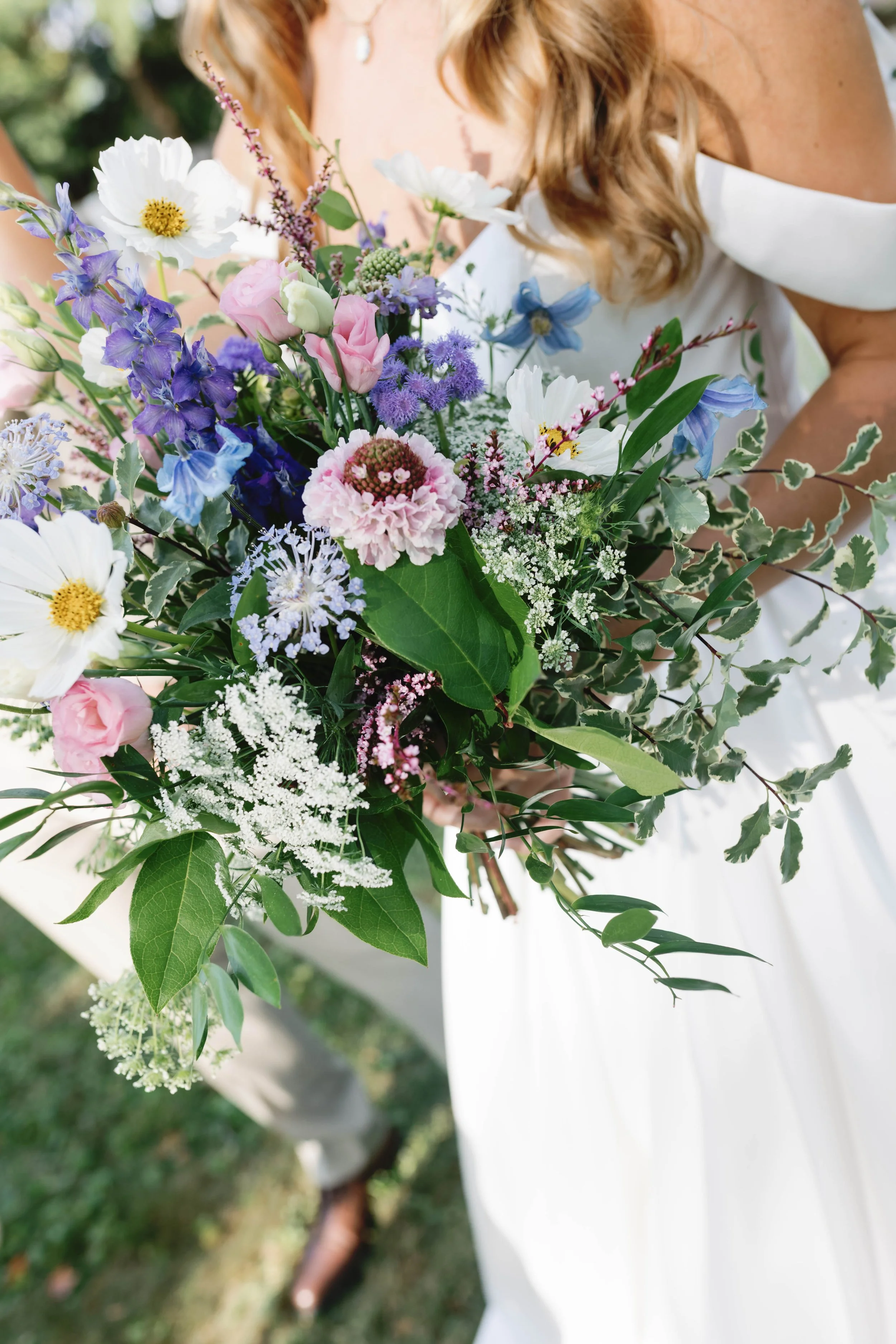 A bride holding a large bouquet of colorful mixed flowers including pink, white, purple, and blue blossoms. kentucky shaker village harrodsburg wedding