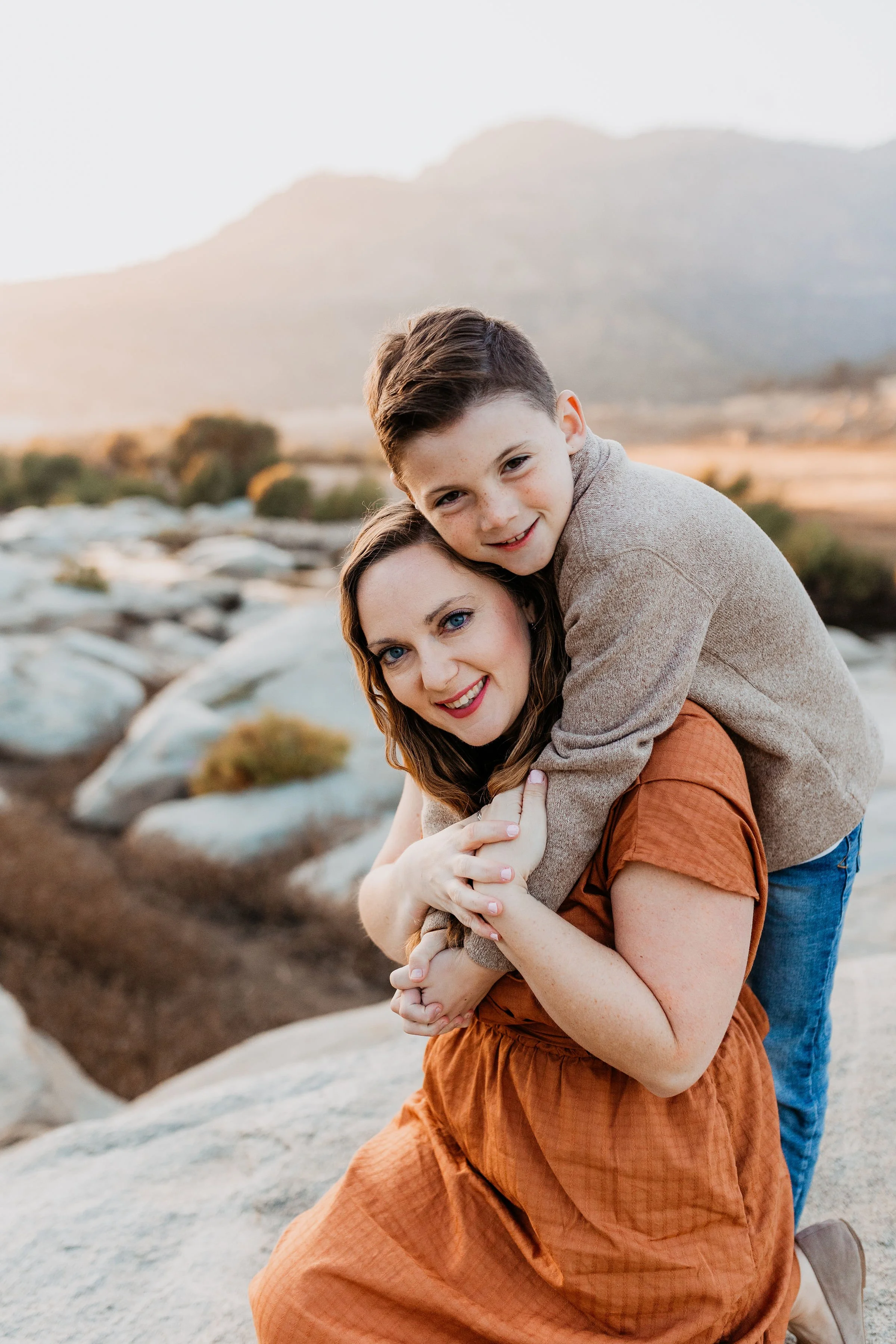 A woman and a young boy embracing outdoors during sunset with mountains and rocks in the background.  lexington kentucky family photographer storytelling portraits