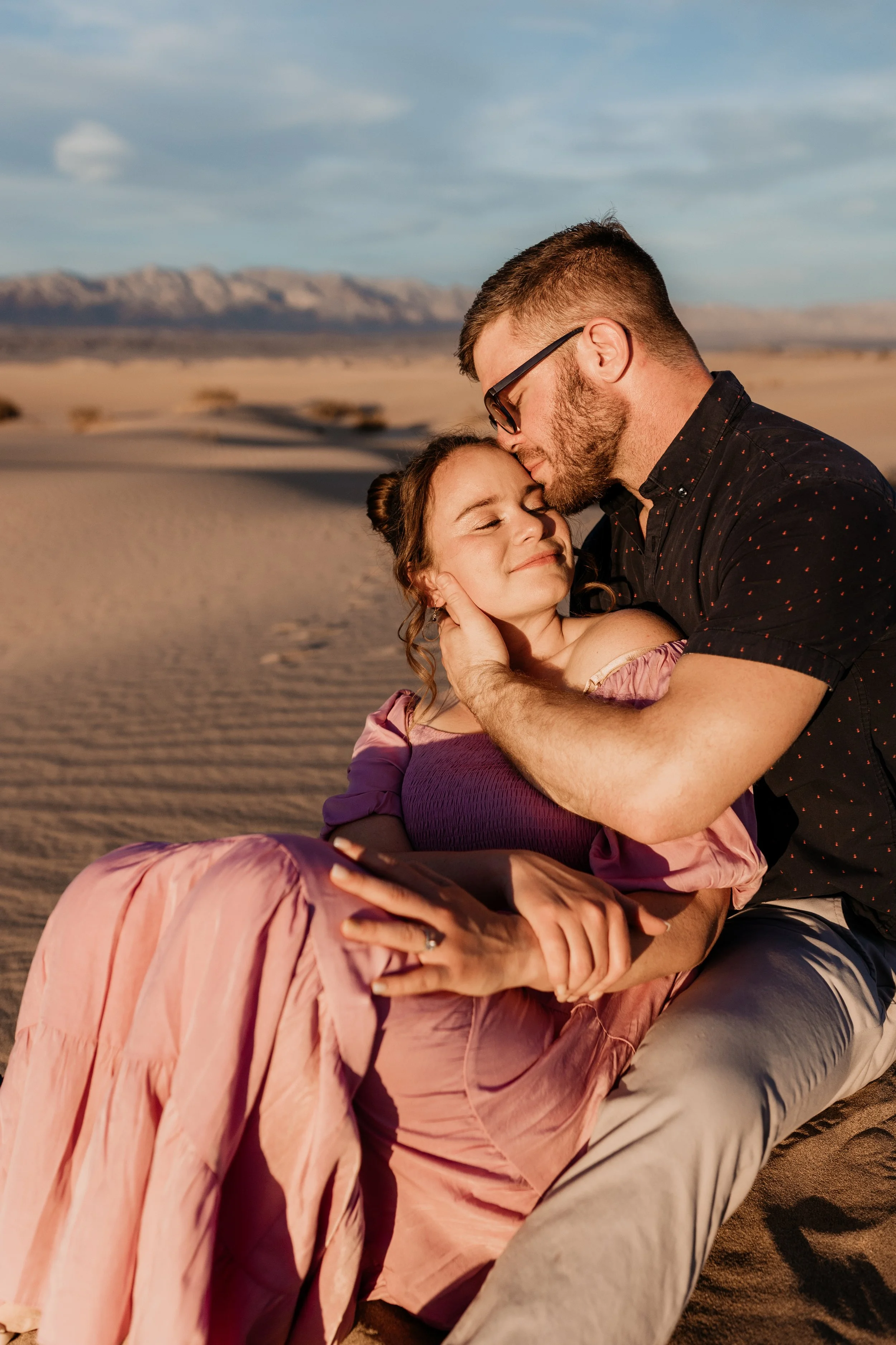 A couple embraces in a desert landscape during sunset, with mountains in the background at death valley national park sand dunes elopement
