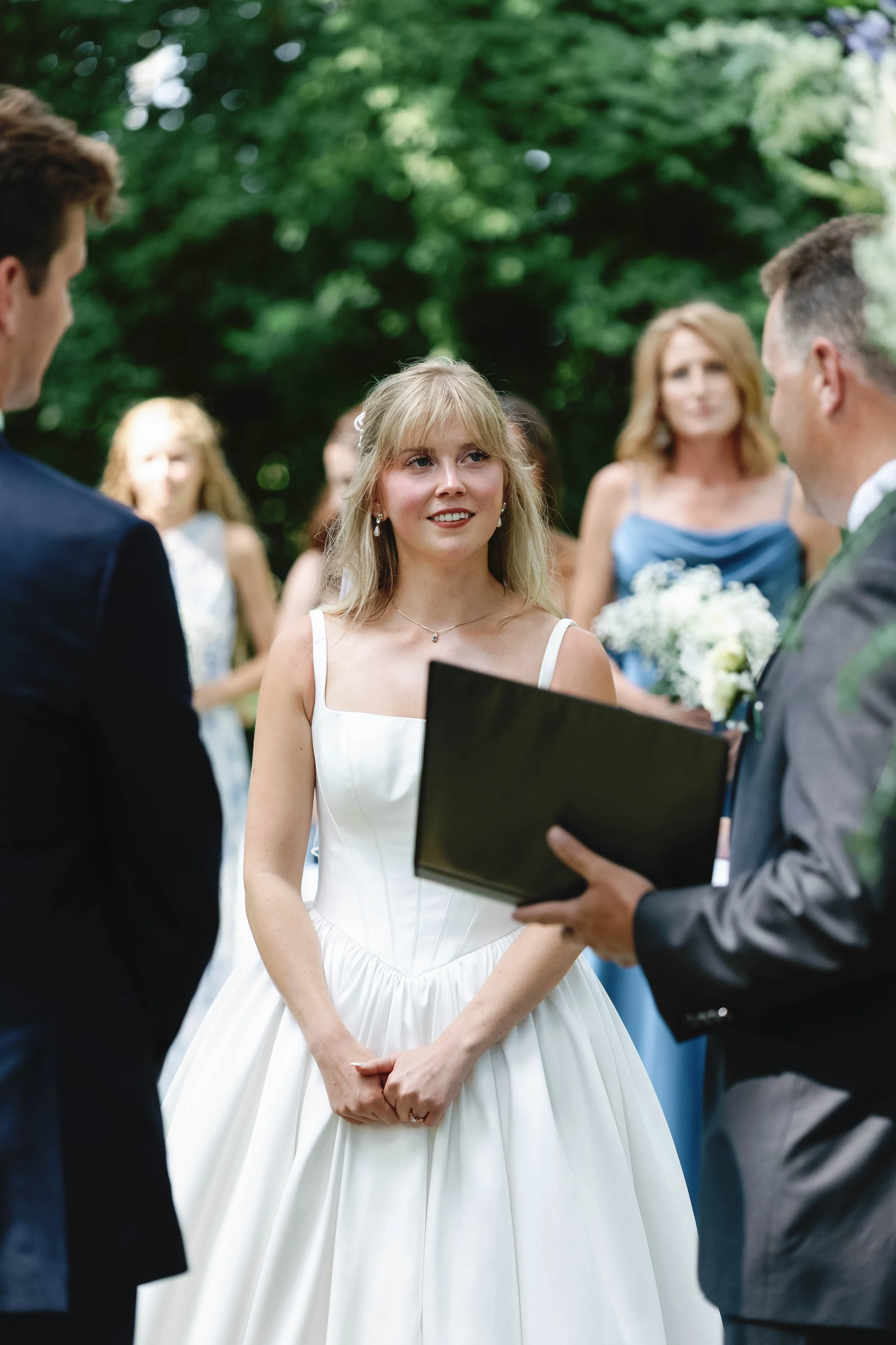 Bride in a white wedding dress during her wedding vows, standing outdoors with bridesmaids and groomsmen in the background. ashford acres inn wedding cynthiana kentucky