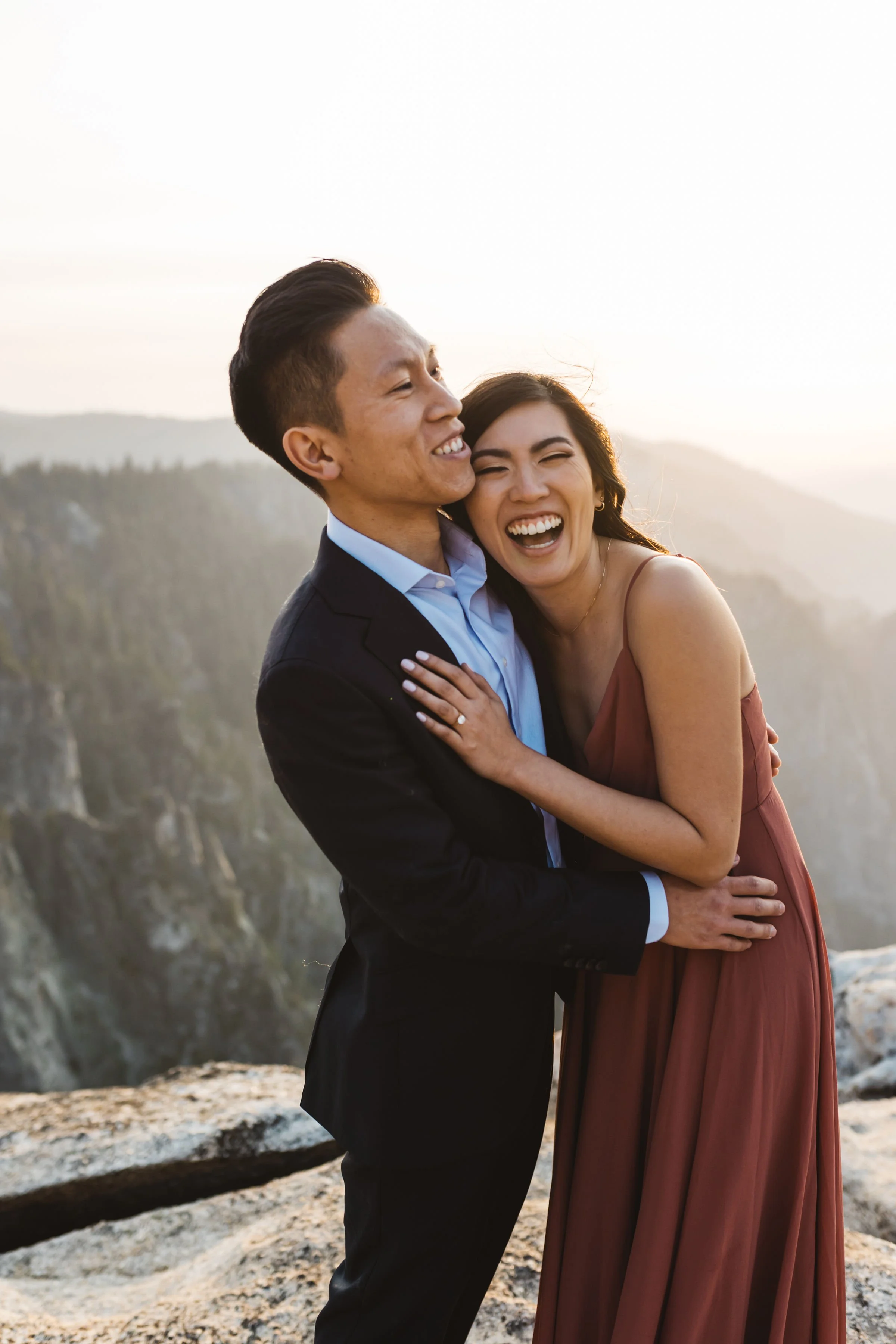 A happy couple embracing outdoors near a rocky cliff at sunset, smiling and laughing taft point yosmite national park elopement