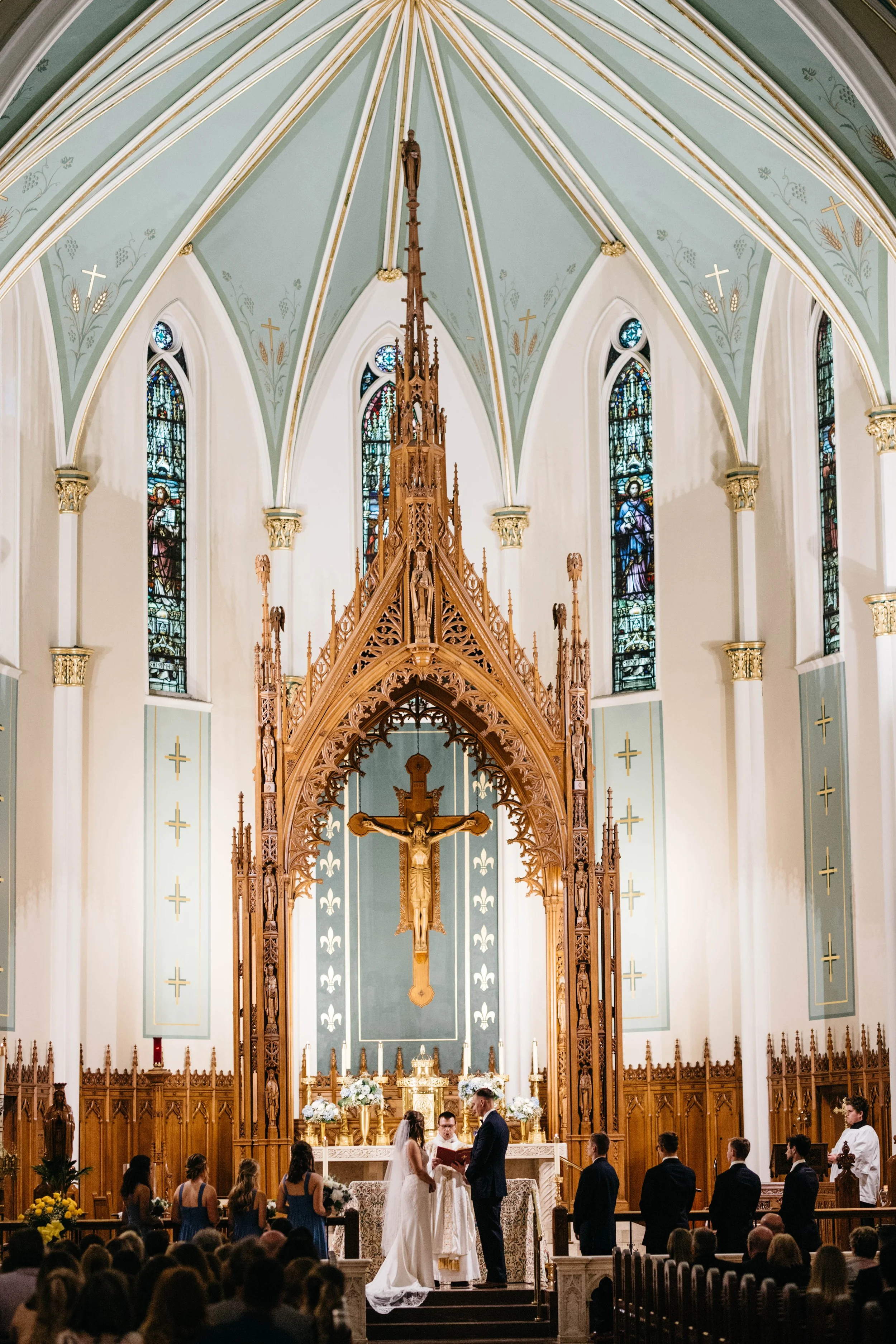 A wedding ceremony taking place in a church with high vaulted ceilings, stained glass windows, and intricate wooden altar decorations. catholic church wedding ceremony kentucky lexington