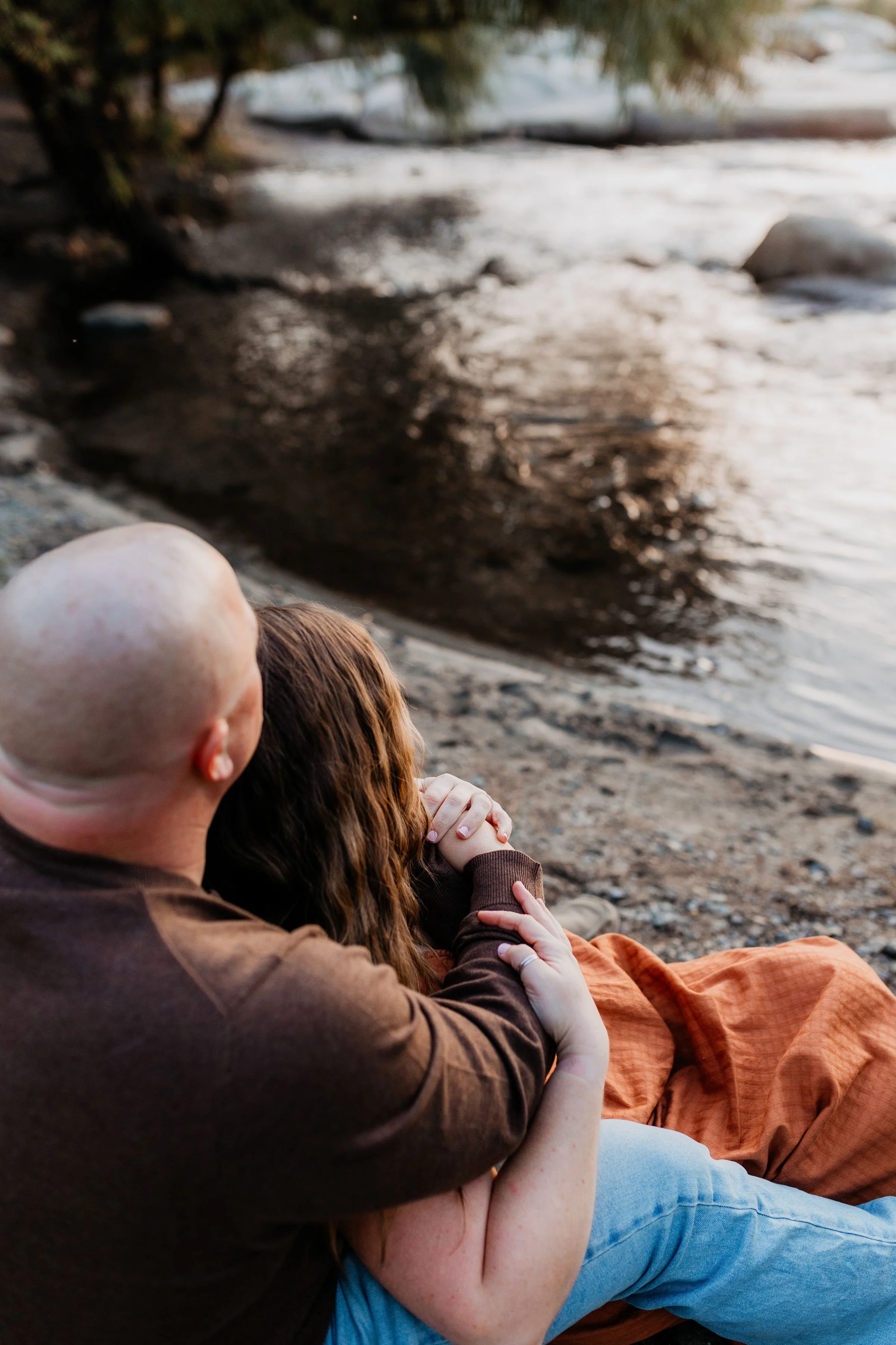 A couple sitting on a beach, embracing and gazing at a river or lake during sunset.  lexington kentucky family photographer storytelling portraits