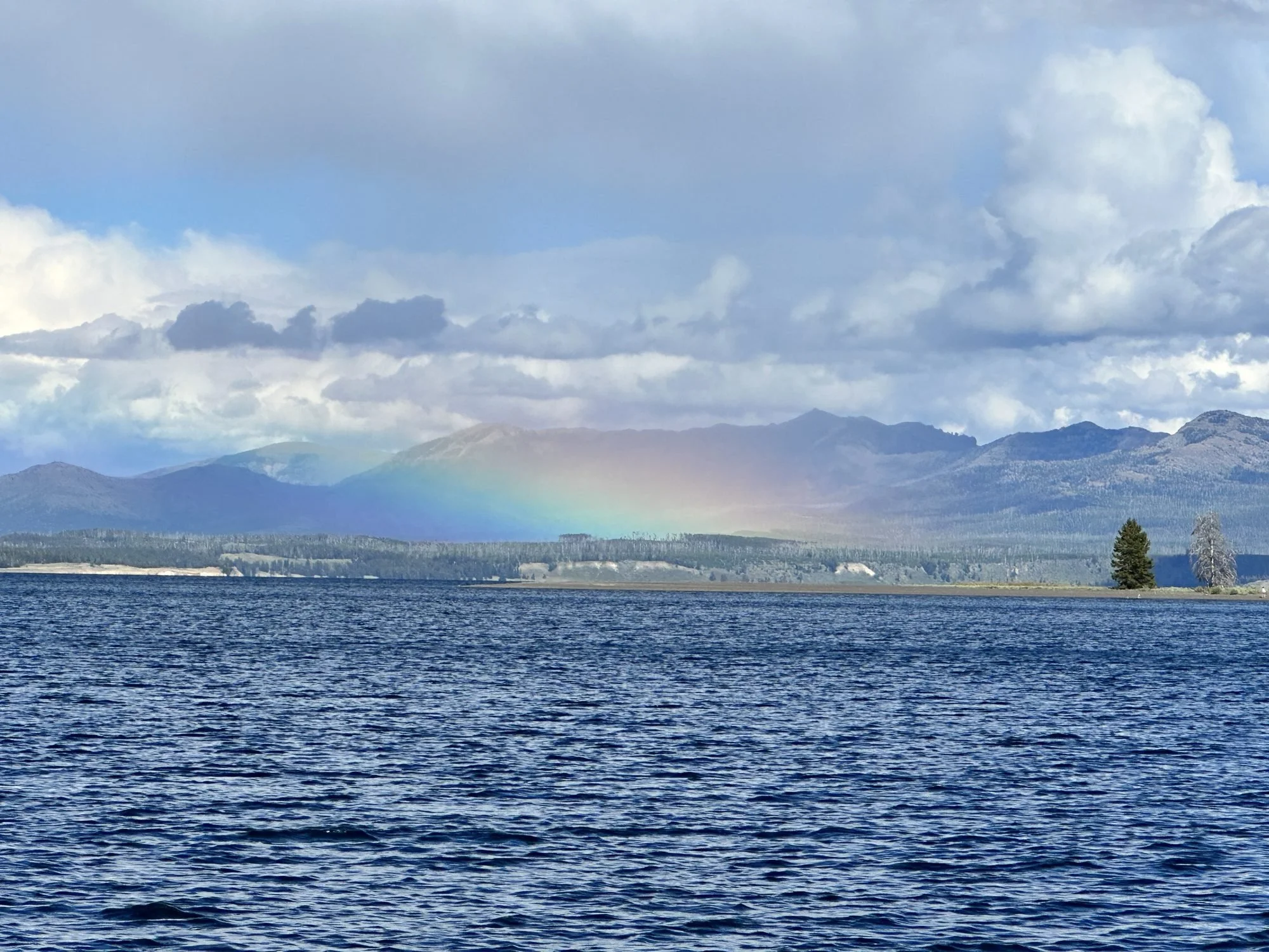 A body of water with gentle waves in the foreground and a mountain range in the background, under a sky filled with clouds, creating a serene landscape.