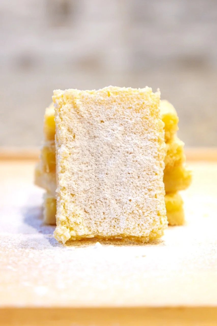Stack of lemon bars dusted with powdered sugar on white surface.