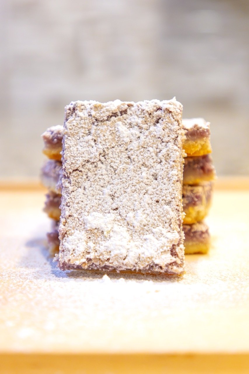 Stacked lemon-berry bars dusted with powdered sugar on a wooden surface.