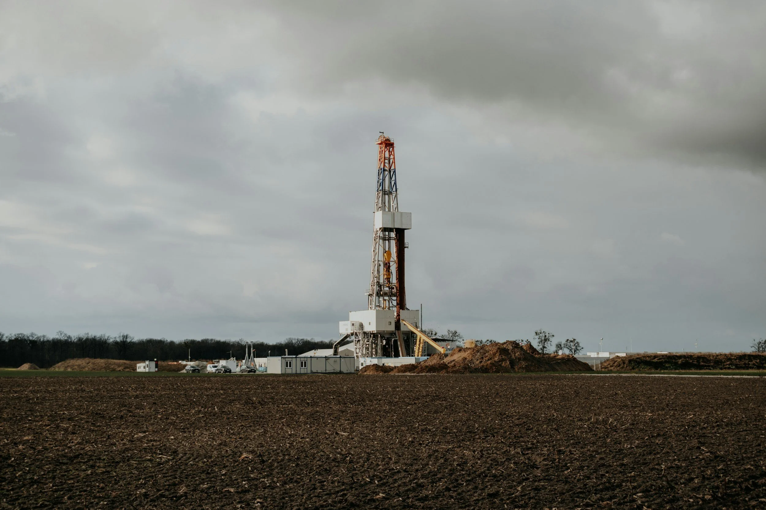 An oil drilling rig standing in a barren field under a cloudy sky.