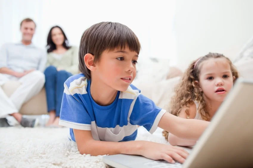 A child and his sister in front of a laptop