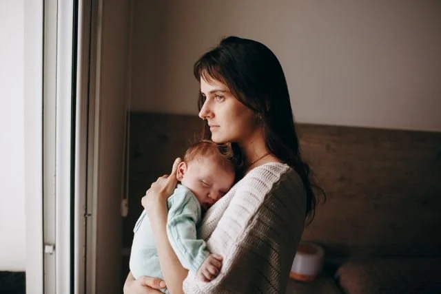 A mom with a newborn looking out a window