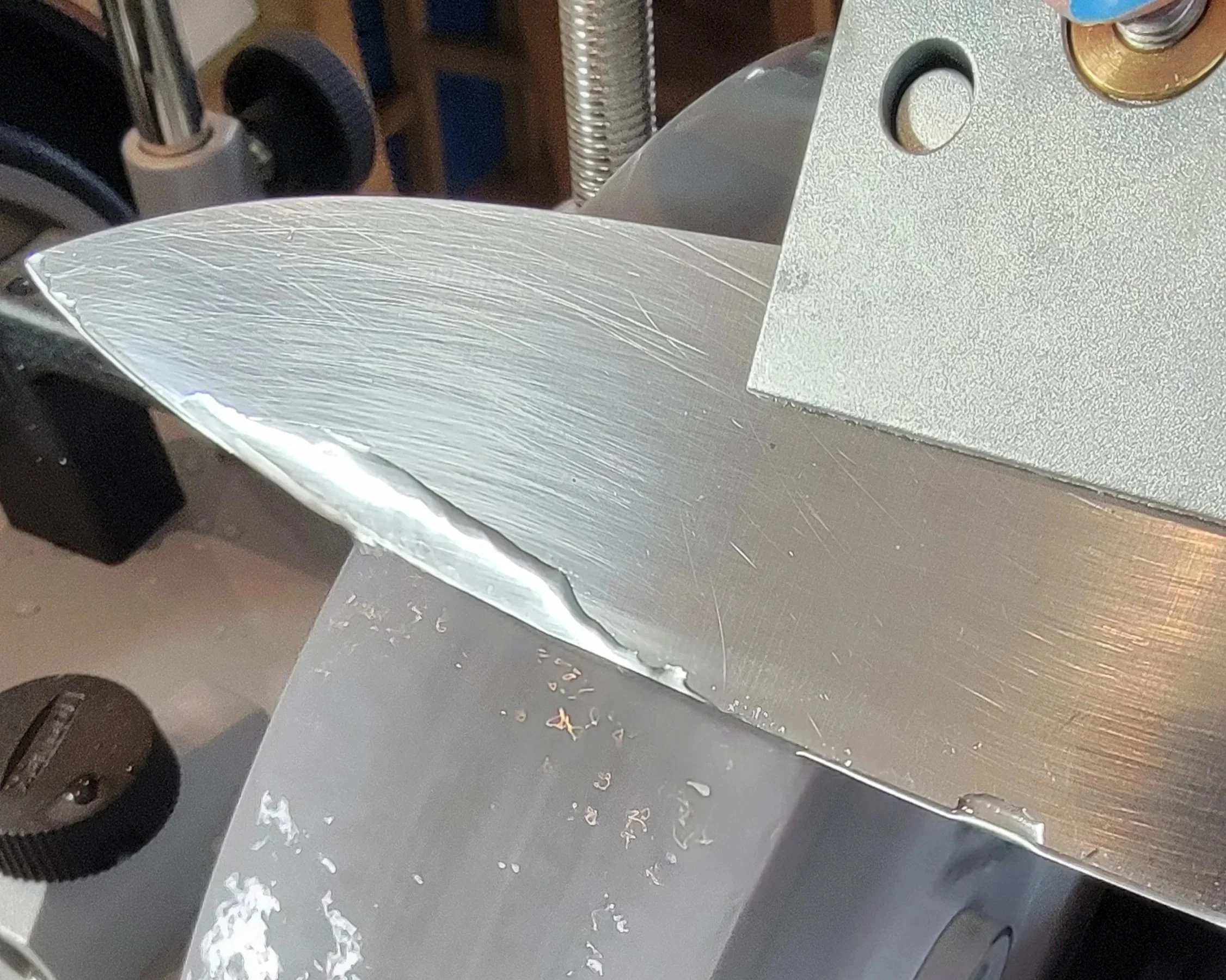 close-up of a metallic blade with visible scratches and a crack, mounted on a machine or tool.