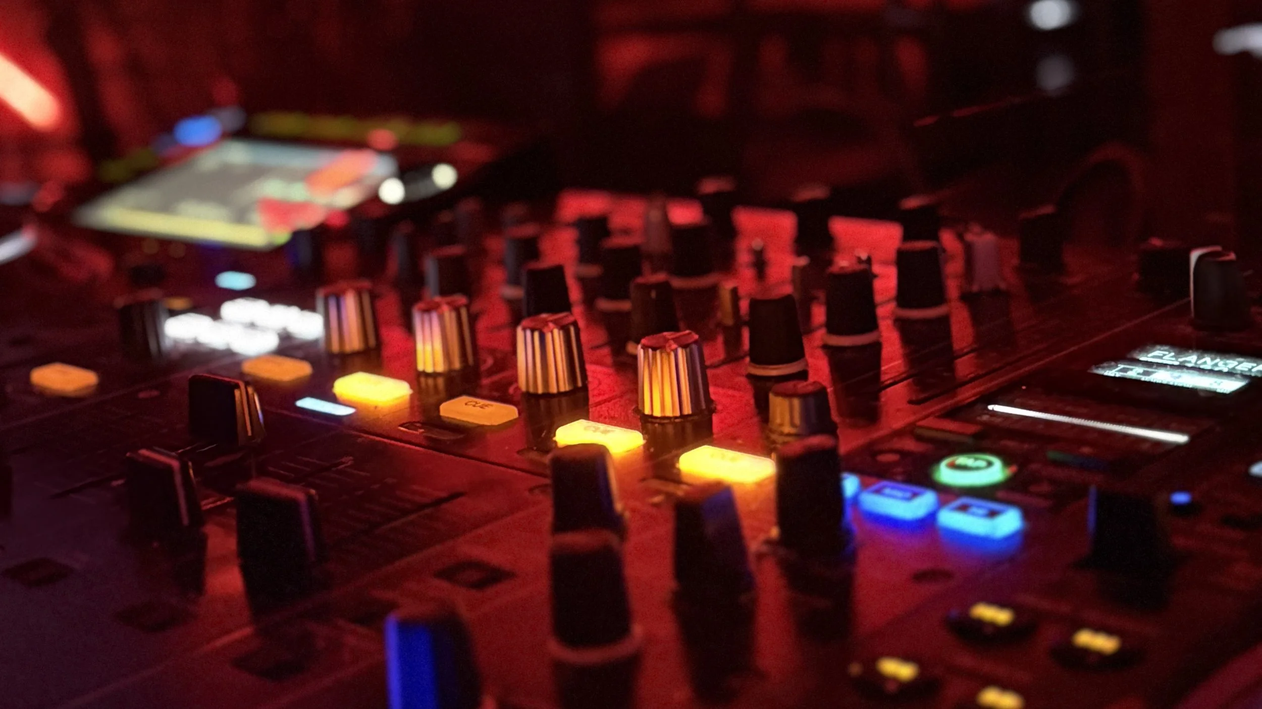 Close-up of a DJ mixing console with illuminated, colorful buttons and knobs in a dark setting.