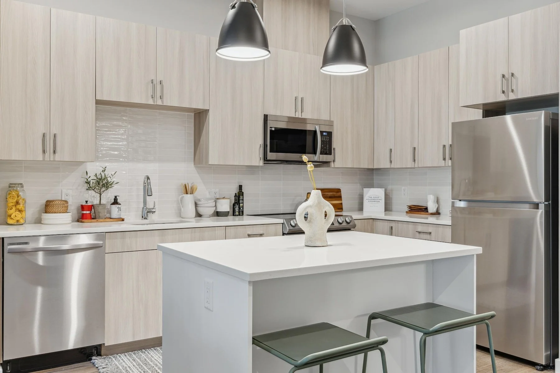 Modern kitchen with white cabinetry, stainless steel appliances, pendant lighting, and a white island with two gray stools.
