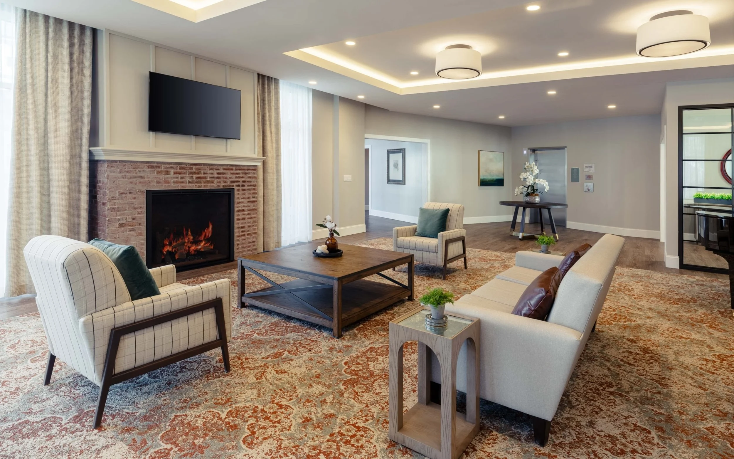 Spacious living room with a brick fireplace, flat-screen TV, sofas, armchairs, a coffee table, and decorative plants.