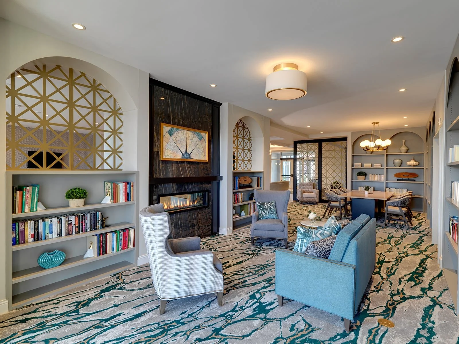 A spacious living room with a modern design featuring a fireplace, bookshelf, and various seating arrangements, including armchairs and a dining table.