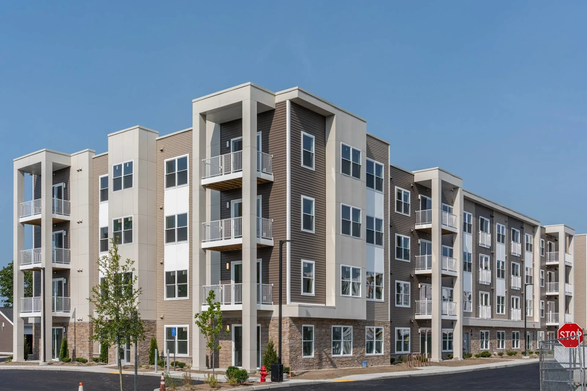Modern, multi-story residential apartment building with balconies and large windows, situated under a clear blue sky.