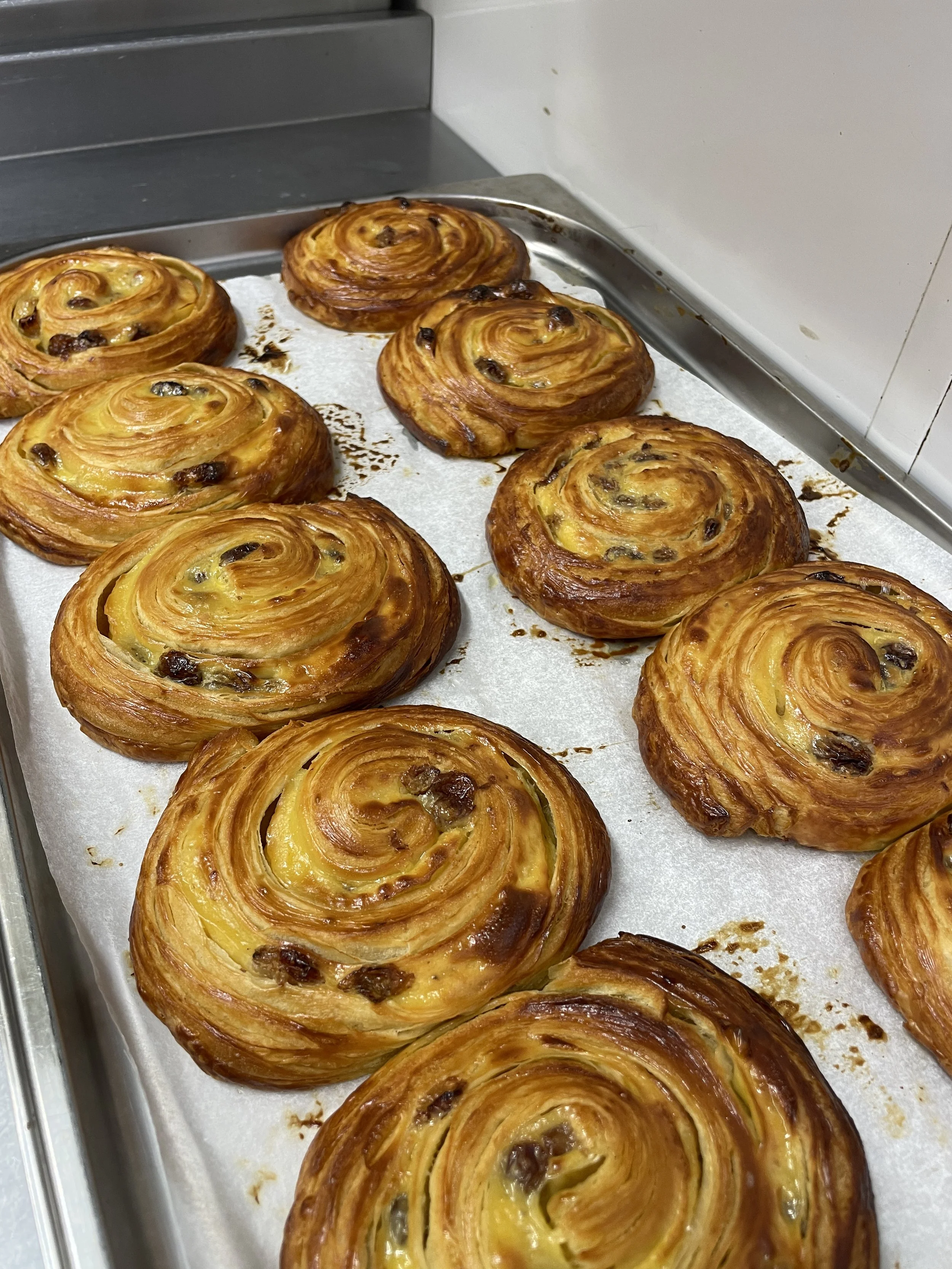 A tray of golden brown pain au chocolat pastries with chocolate chips, fresh out of the oven.