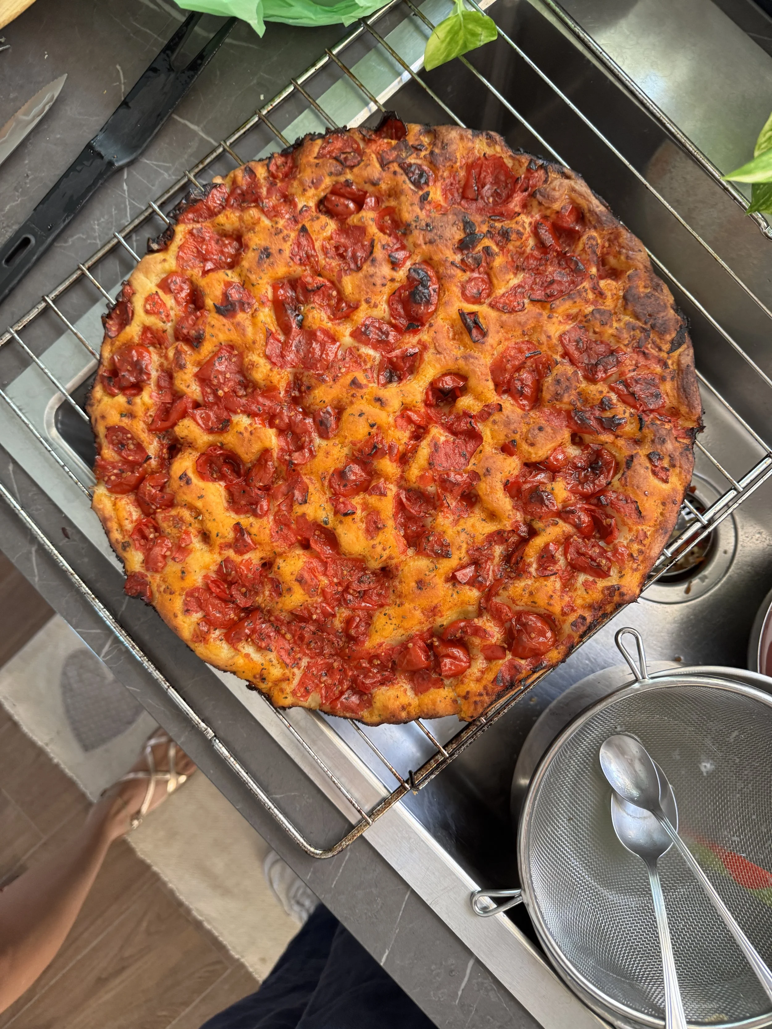 A freshly baked pizza topped with cherry tomatoes on a cooling rack over a kitchen countertop.