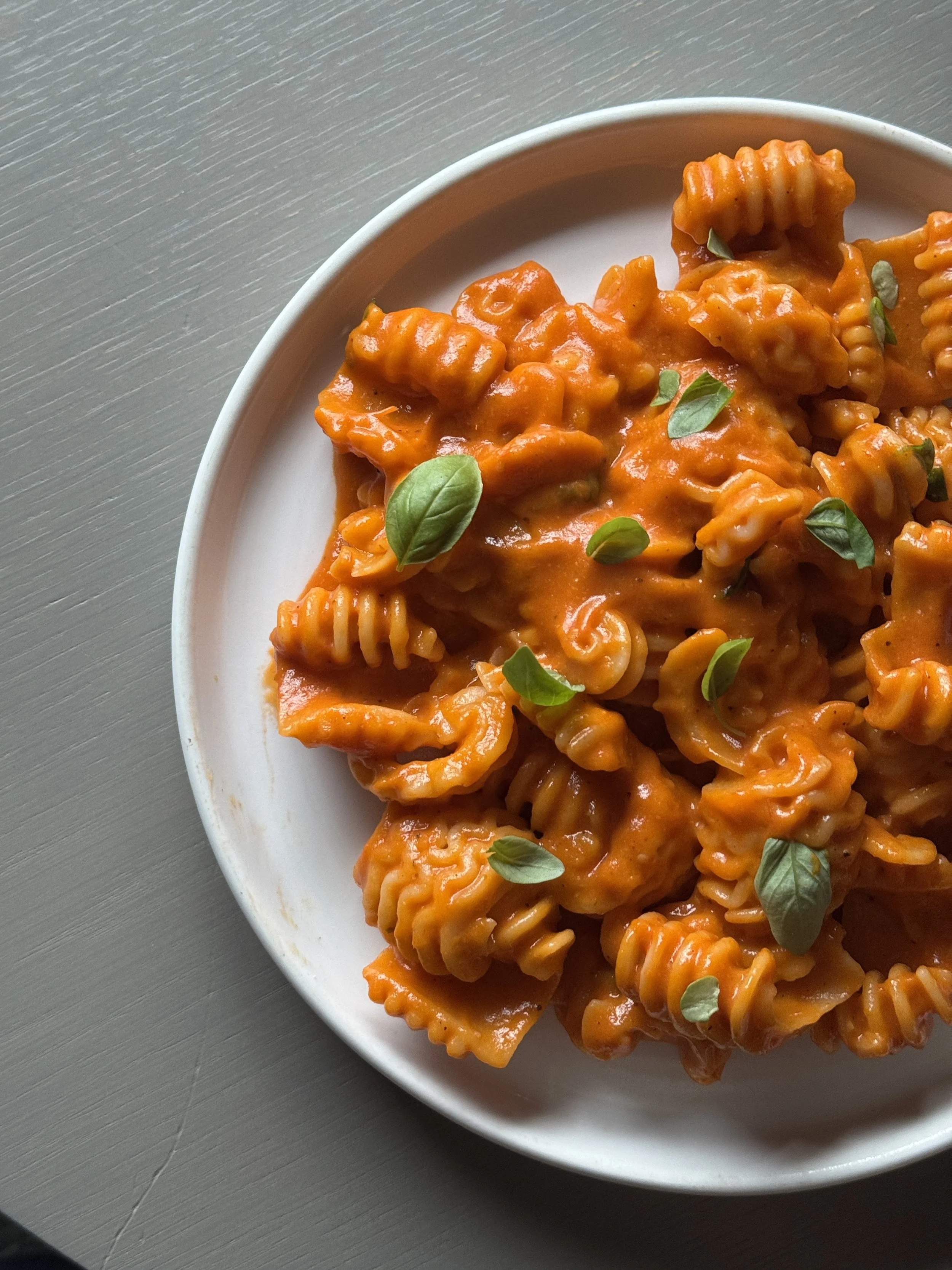 A white plate of rotini pasta with tomato sauce garnished with fresh basil leaves.