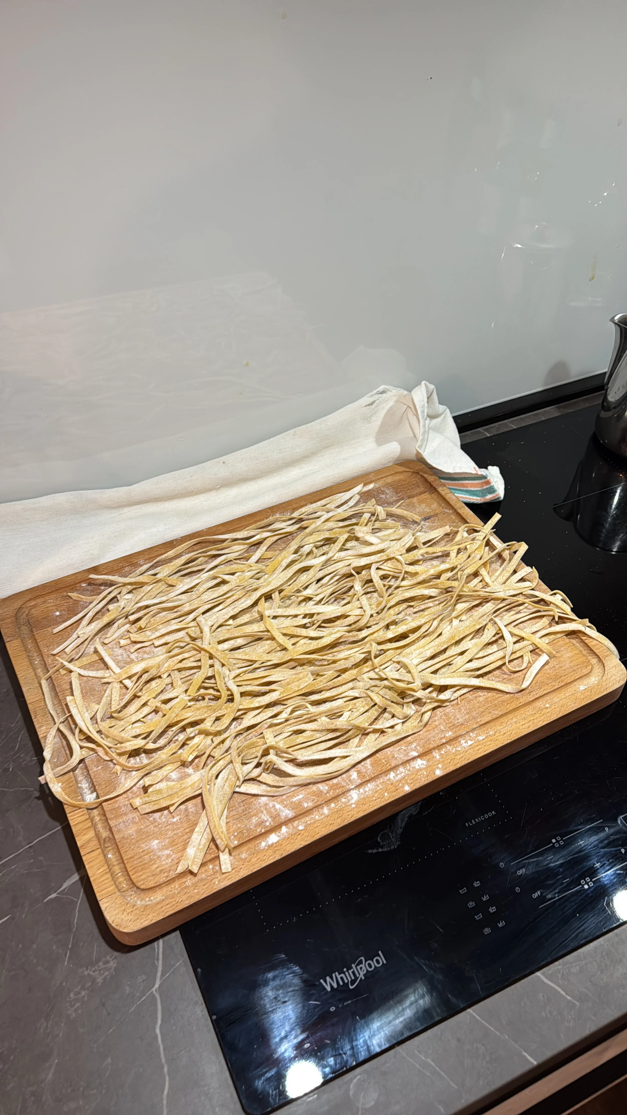 Fresh homemade pasta laid out on a wooden cutting board on a black countertop in a kitchen.