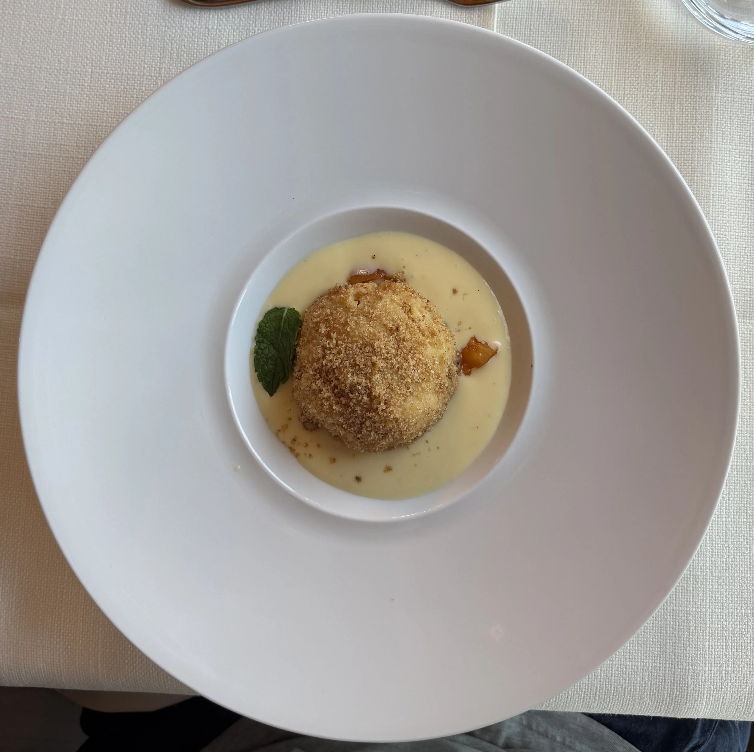 A breaded, fried ball served on a bed of creamy sauce with a mint leaf garnish on a white plate.