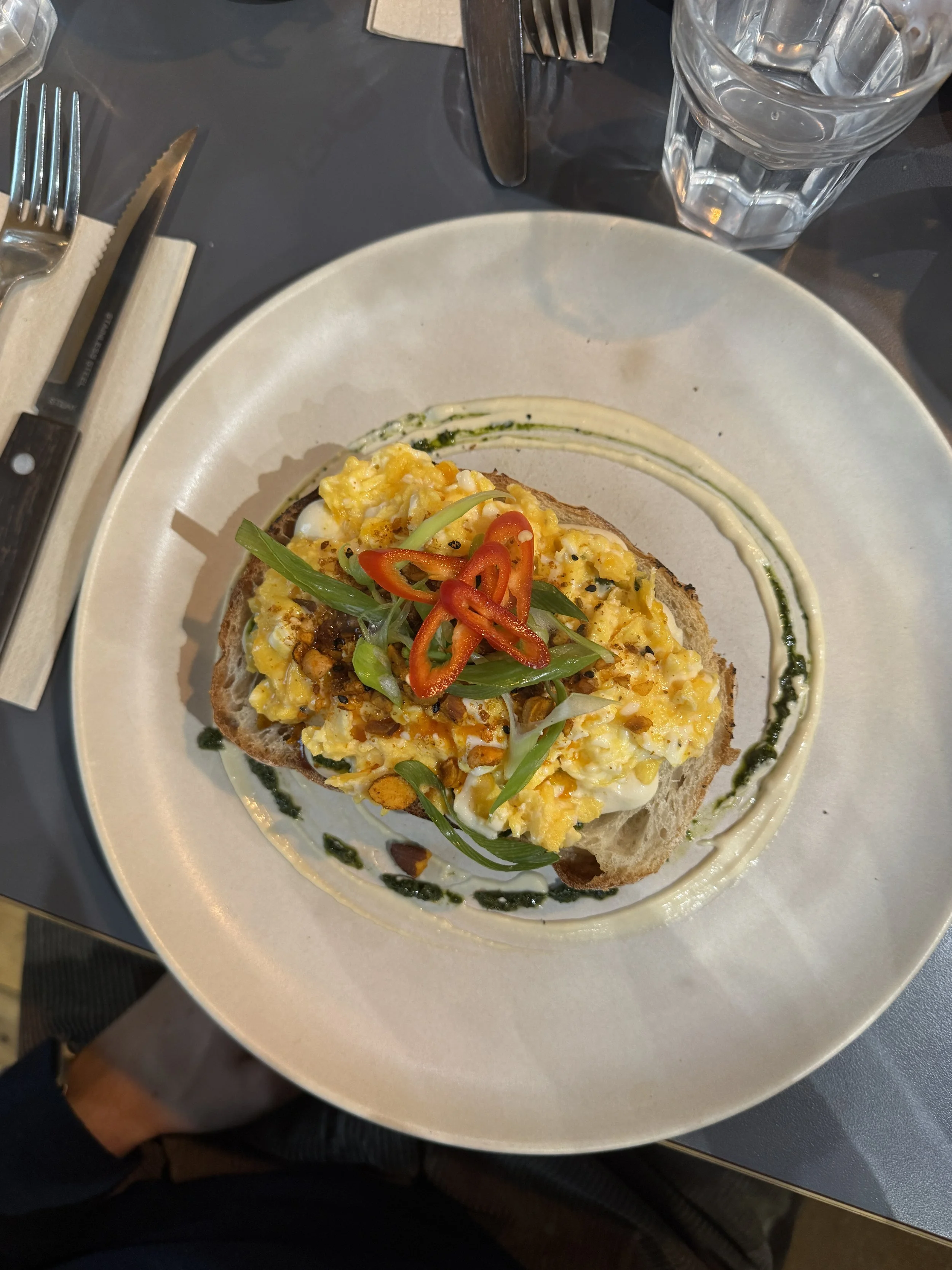 Open-faced sandwich topped with scrambled eggs, sliced red chili peppers, and green onion, garnished with green sauce on a white plate.