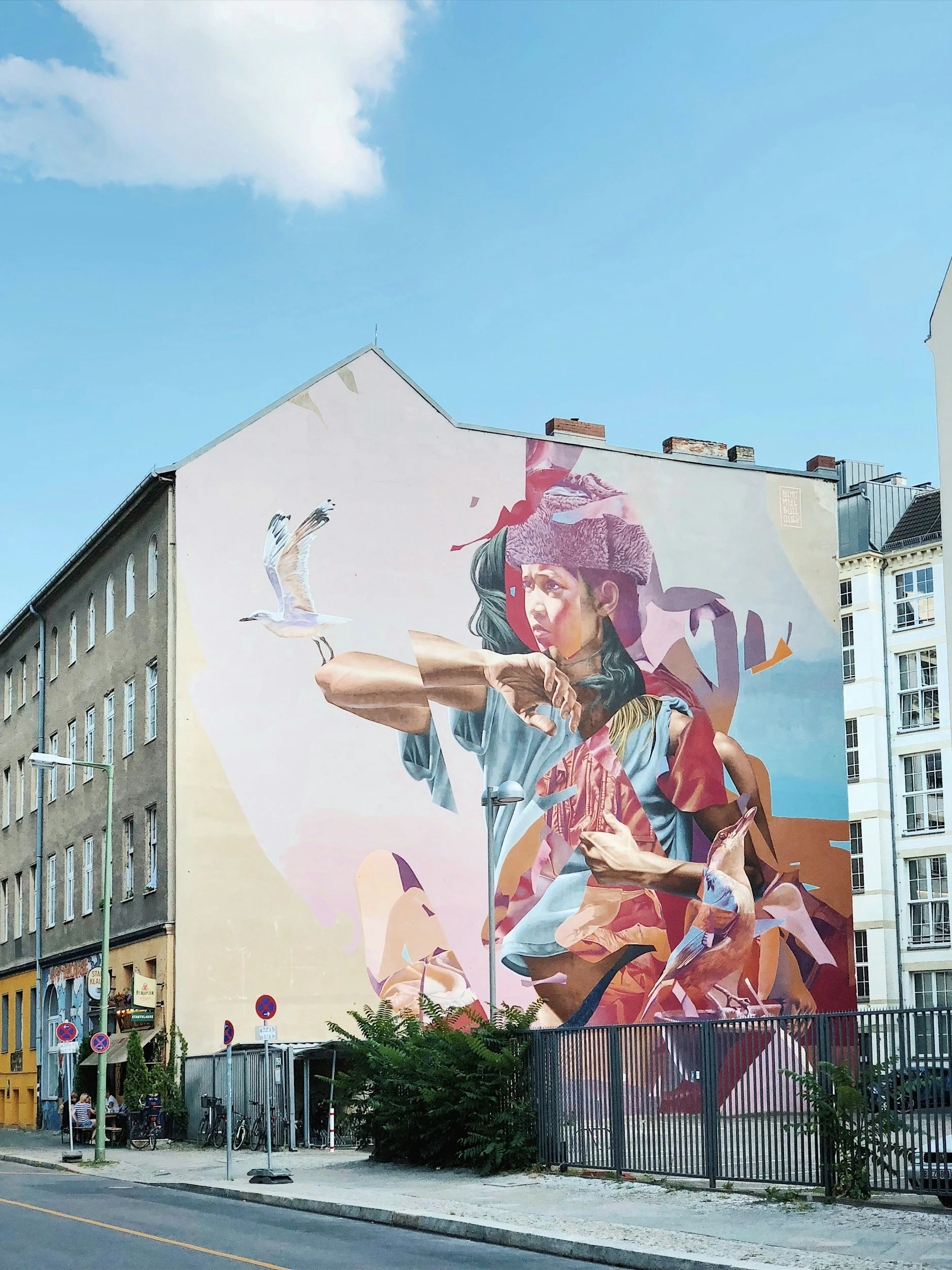 Large mural depicting a woman with long hair wearing a headscarf, surrounded by abstract shapes and a flying seagull, painted on the side of a building.