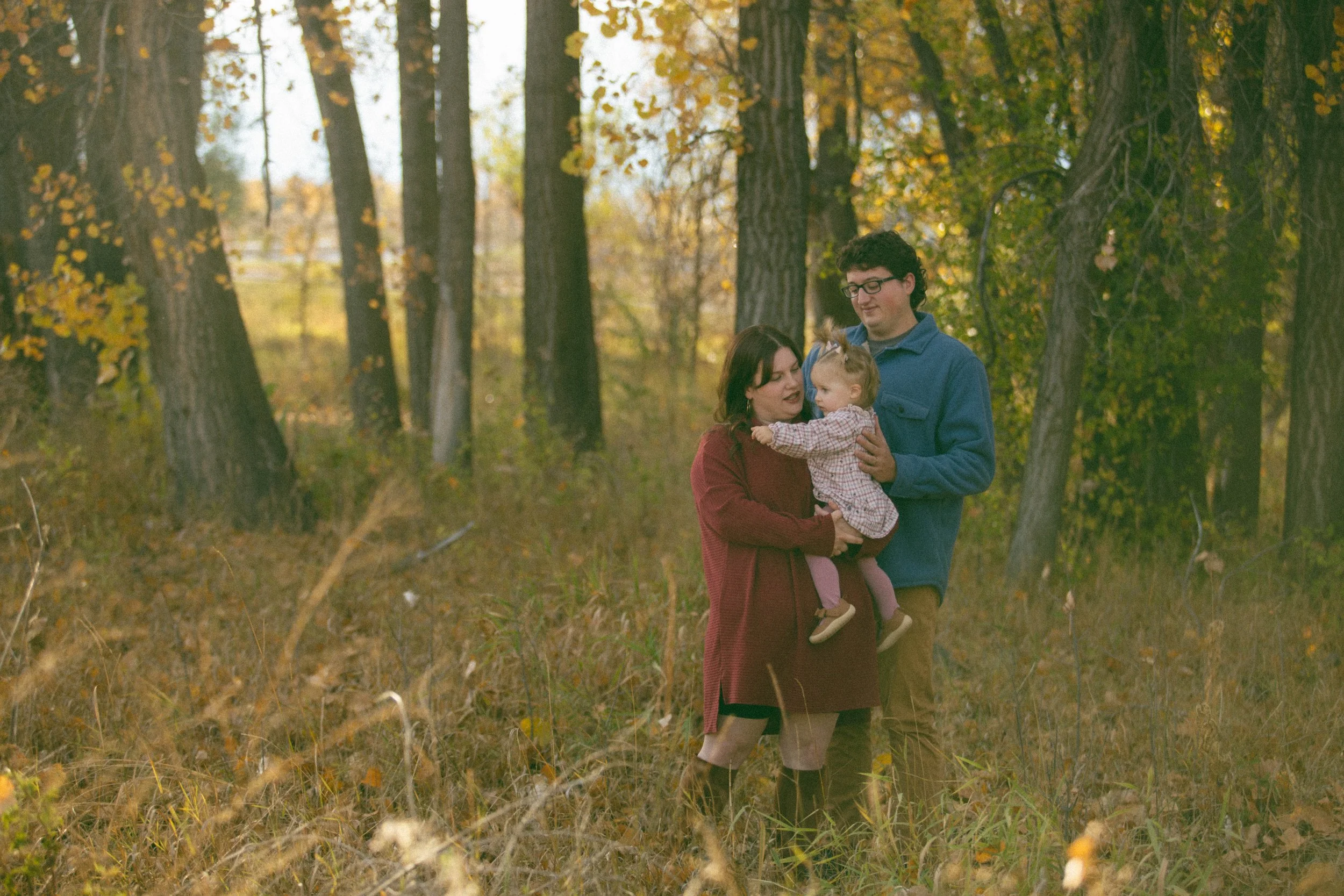 A family of three, a woman, man, and young girl, enjoying an autumn walk in a wooded area with fall foliage.