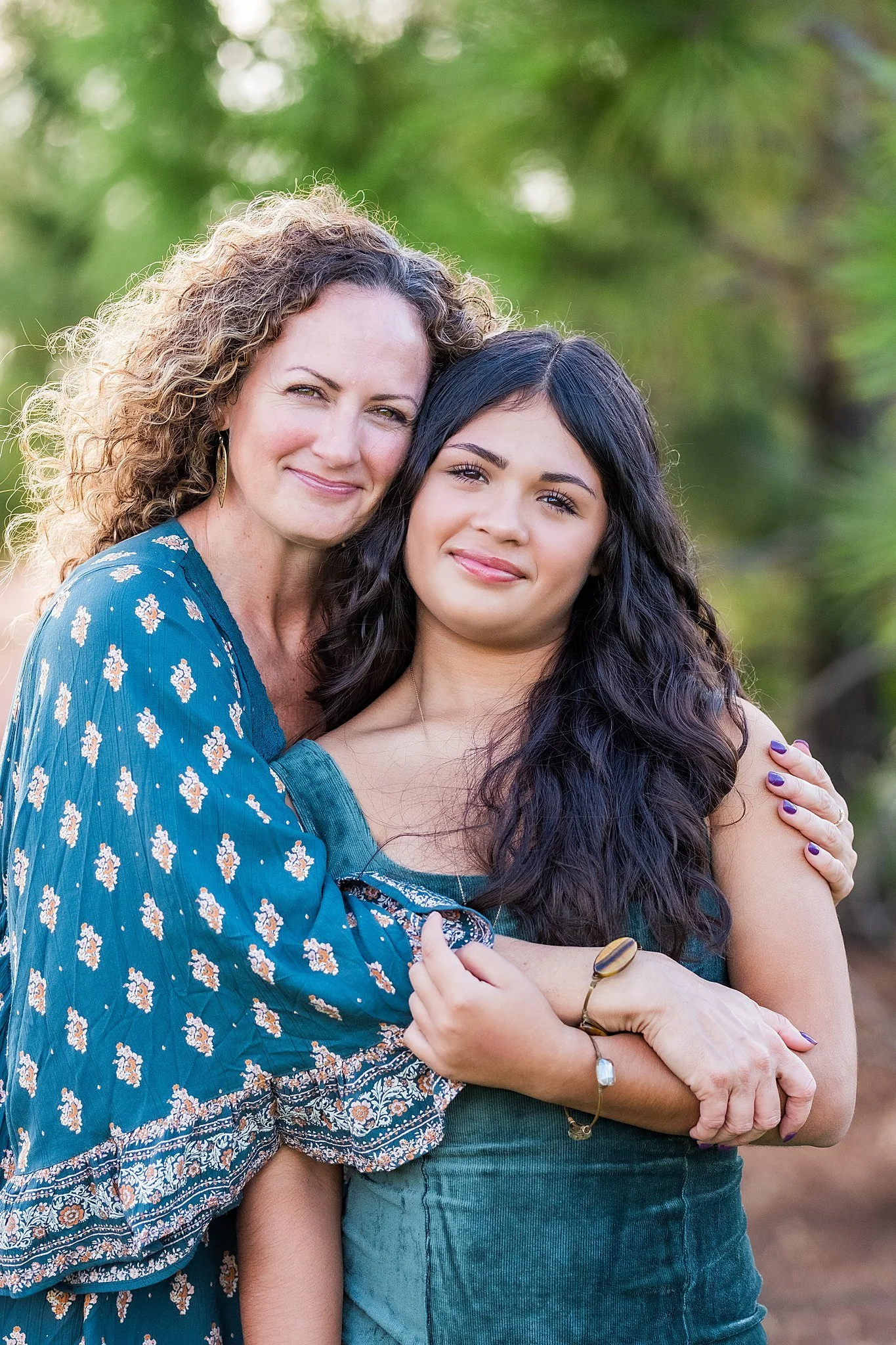 Mother and daughter embracing outdoors with green foliage background.