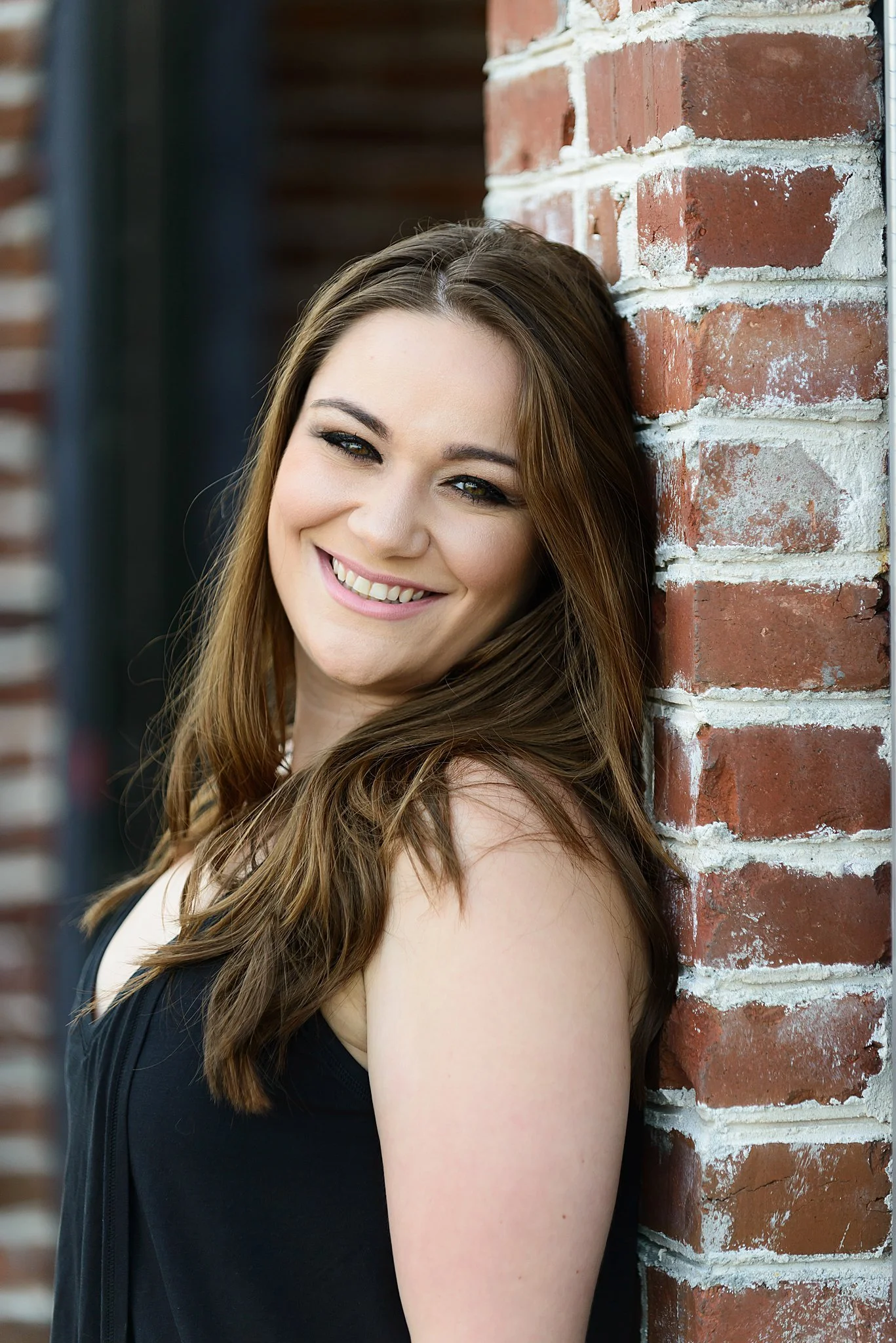 Smiling woman leaning against a brick wall.