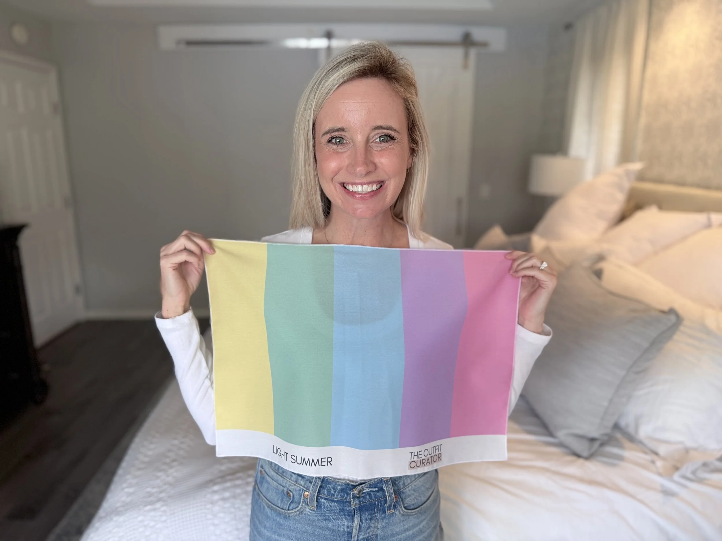 A woman smiling and holding a color palette with pastel shades labeled 'Light Summer' inside a bedroom.