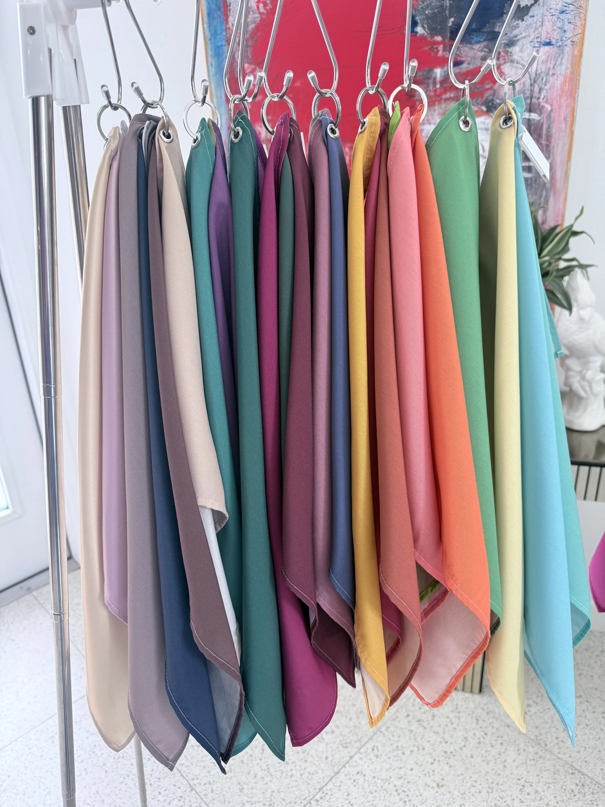 A clothing rack with colorful folded towels or cloths hanging on hooks, arranged in a rainbow spectrum from beige to blue.