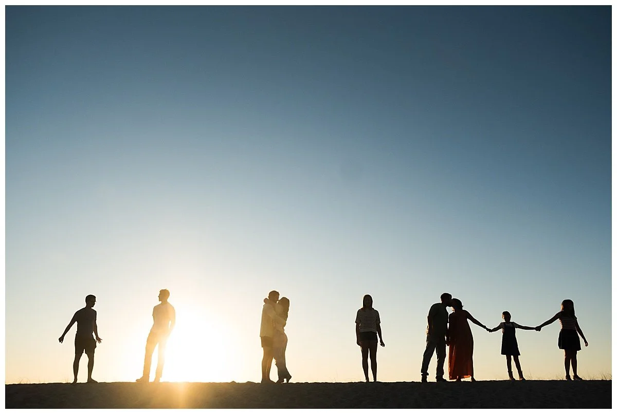 Silhouettes of people holding hands and embracing against a sunset sky.