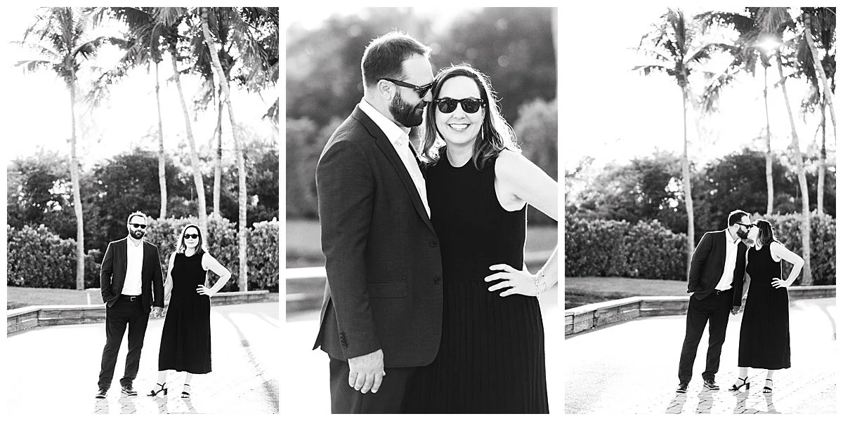 Black and white photo of a couple in an outdoor park with palm trees, the man wearing a suit and glasses, the woman wearing a sleeveless dress and sunglasses, standing close and smiling.