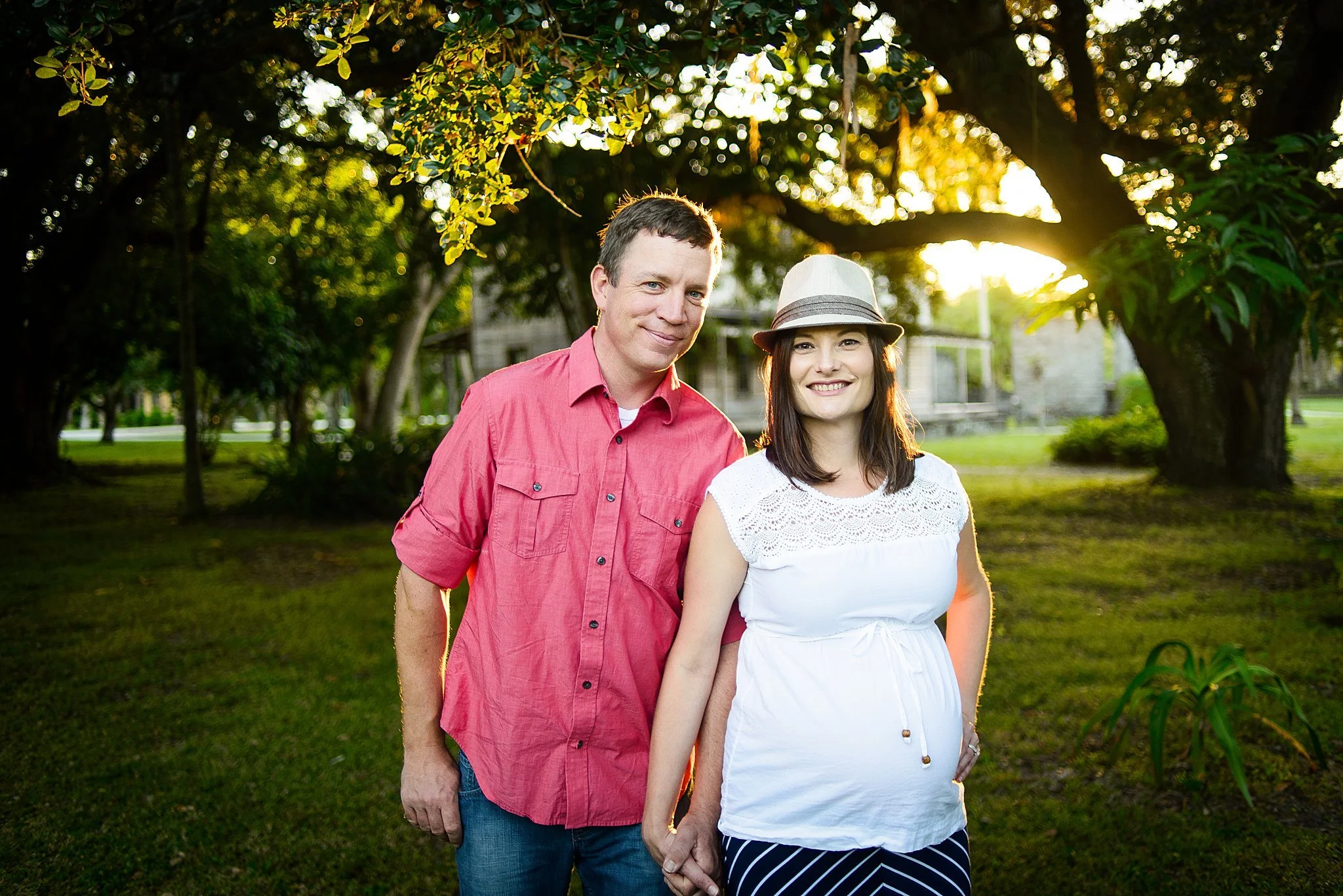 A smiling couple holding hands in a park during sunset, with trees and a grassy area in the background.