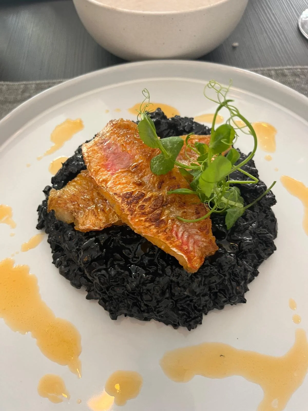 Seared fish fillet served on a bed of black rice with a drizzle of sauce and garnished with microgreens.