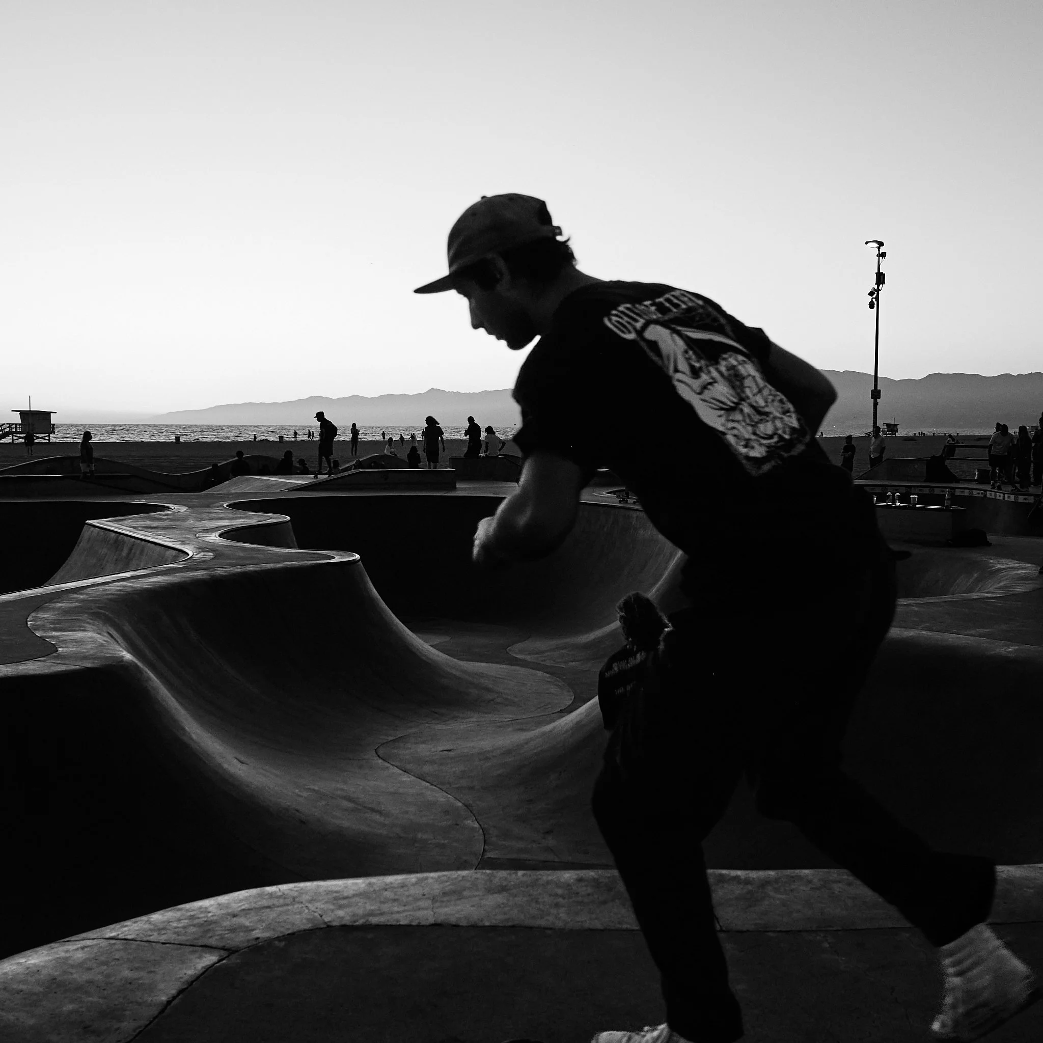 Silhouette of a person at a skate park during sunset with a view of the ocean and mountains in the background.