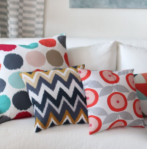 Four decorative pillows with different colorful patterns on a white sofa.