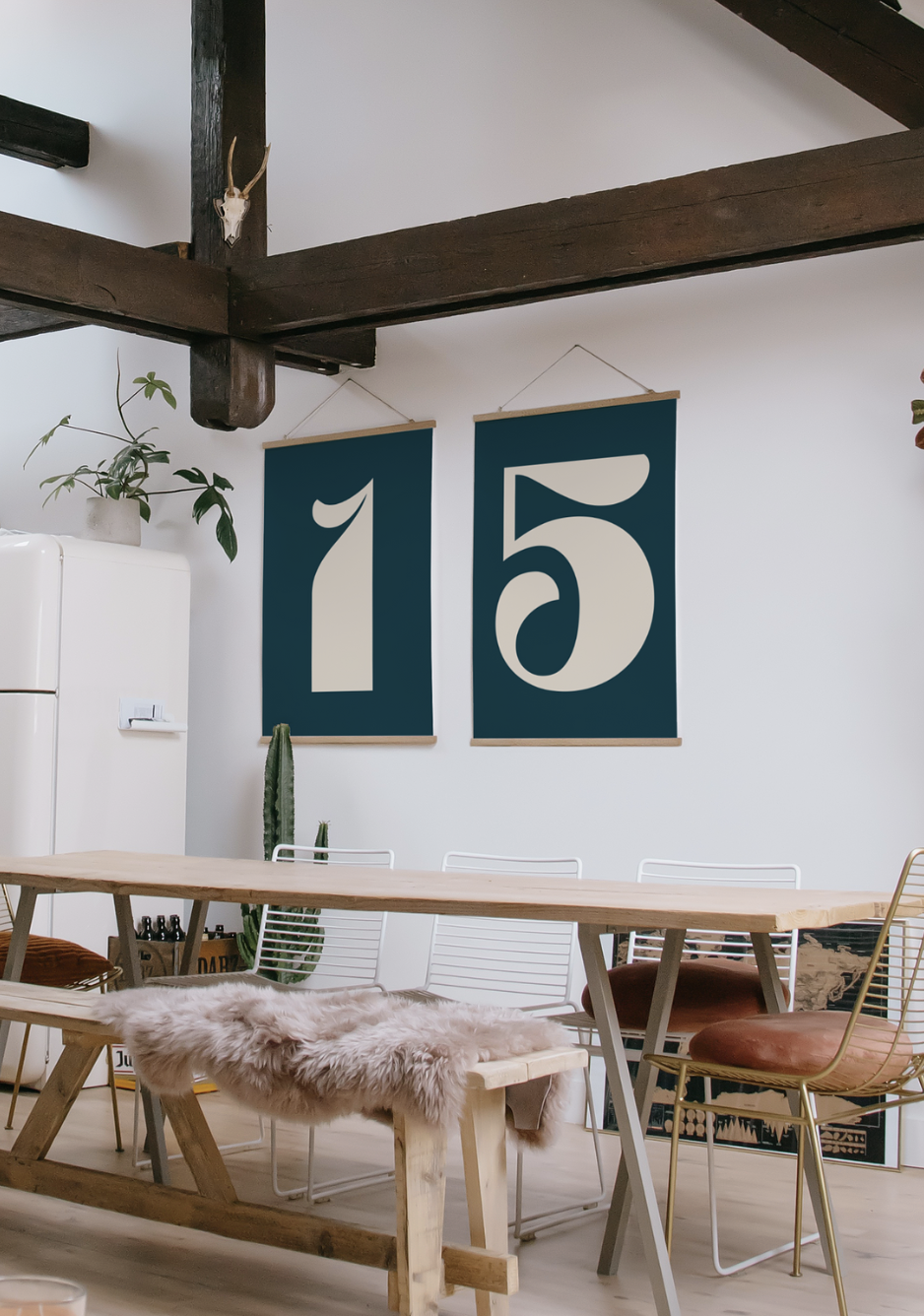 Interior of a modern dining room with a wooden table, wire chairs, and a bench with a faux fur throw, decor includes large teal banners with the number 15, a cactus, a potted plant, and a white retro-style refrigerator, with dark wooden beams and a m