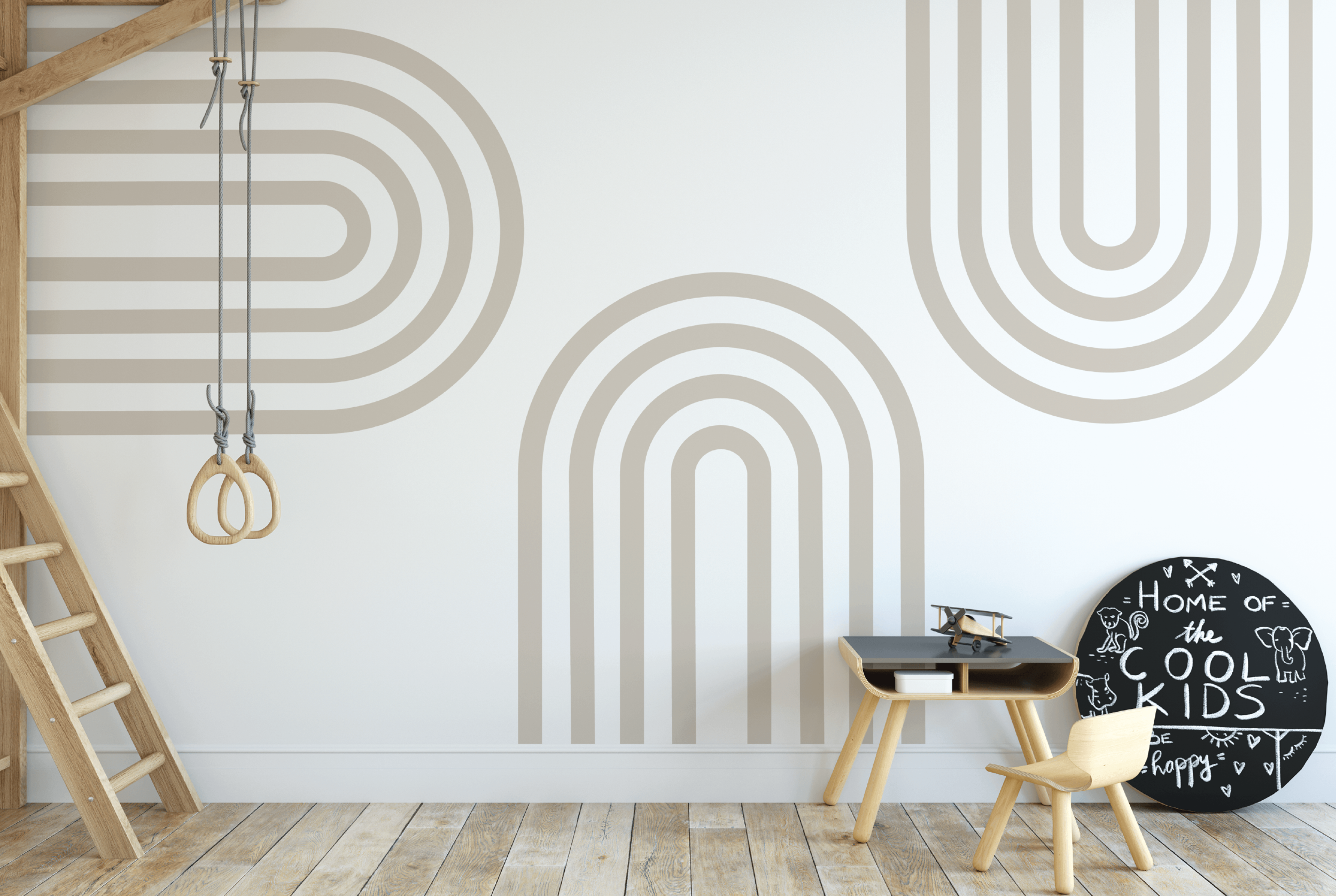Child's playroom with gymnastic rings hanging from the ceiling, a wooden ladder on the left, a small black desk with a toy airplane on top, a wooden chair, and a round black chalkboard sign that says "Home of the Cool Kids" with playful drawings and 