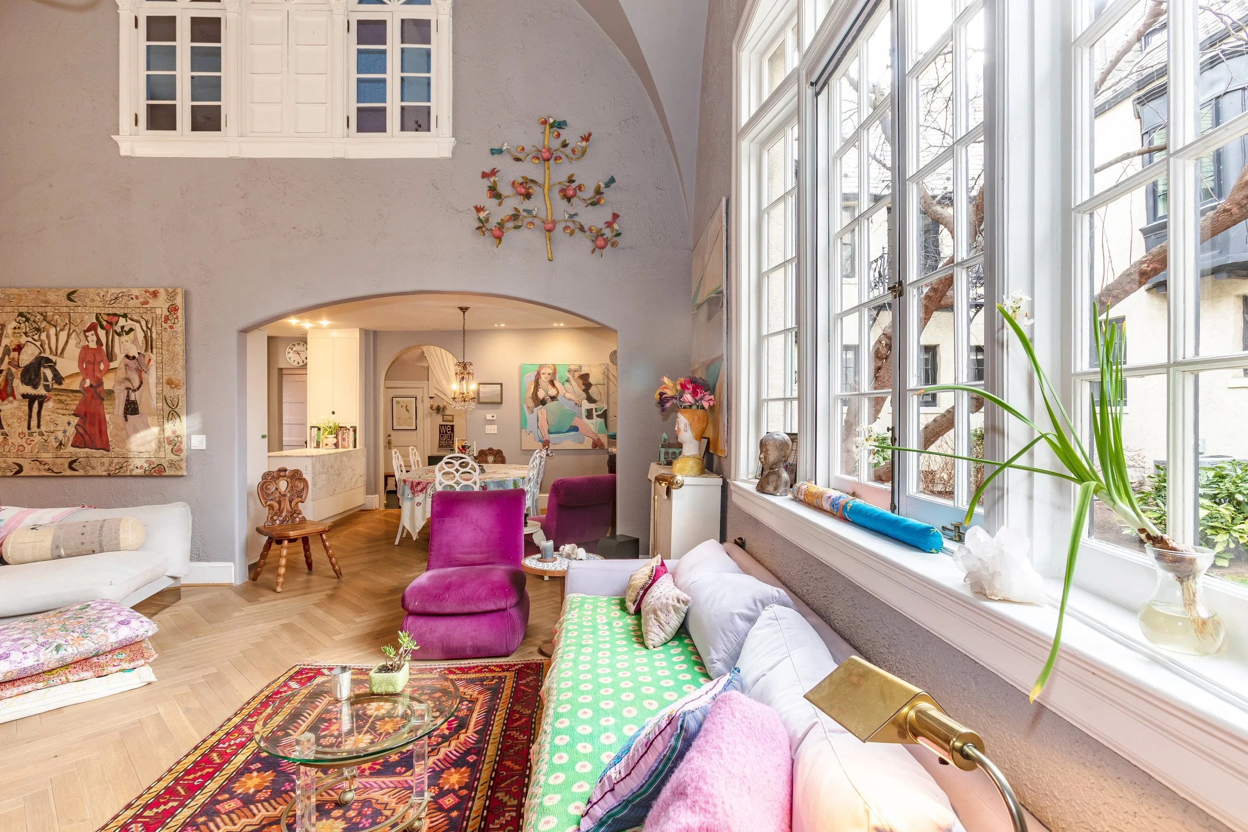 Bright living room with large windows, colorful furniture, wall art, and decorative objects.